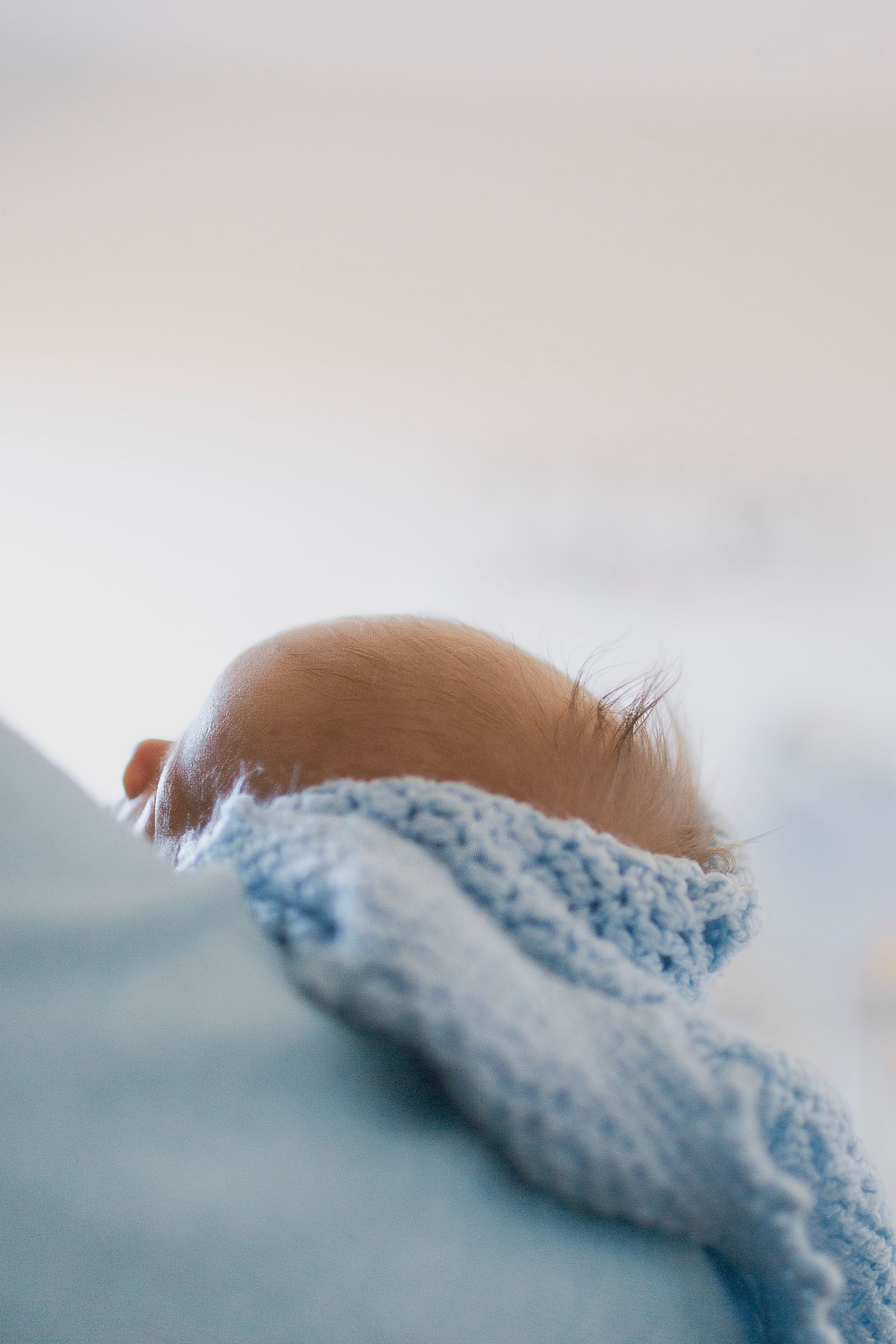 Close-up of a newborn baby's head wrapped in a soft blue knitted blanket.