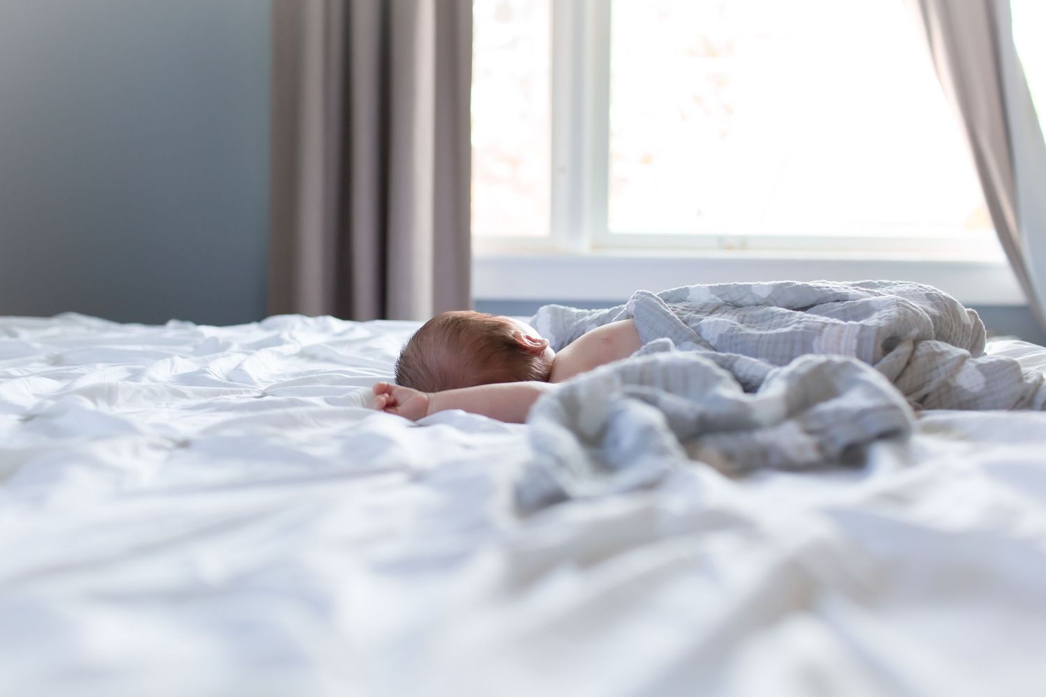 A cozy unmade white bed with rumpled sheets and blankets near a window in natural daylight.