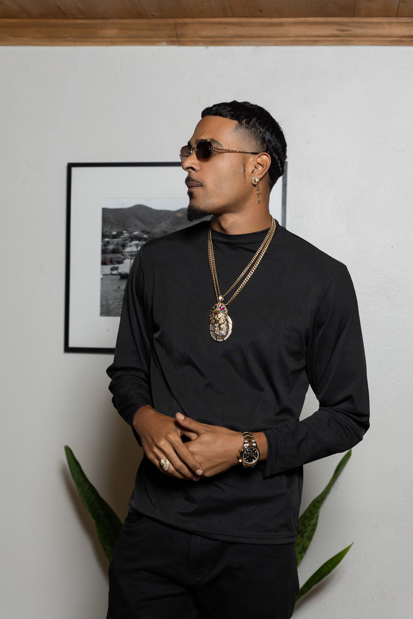 Stylish man in black long-sleeve shirt with gold chain necklace and sunglasses posing indoors.