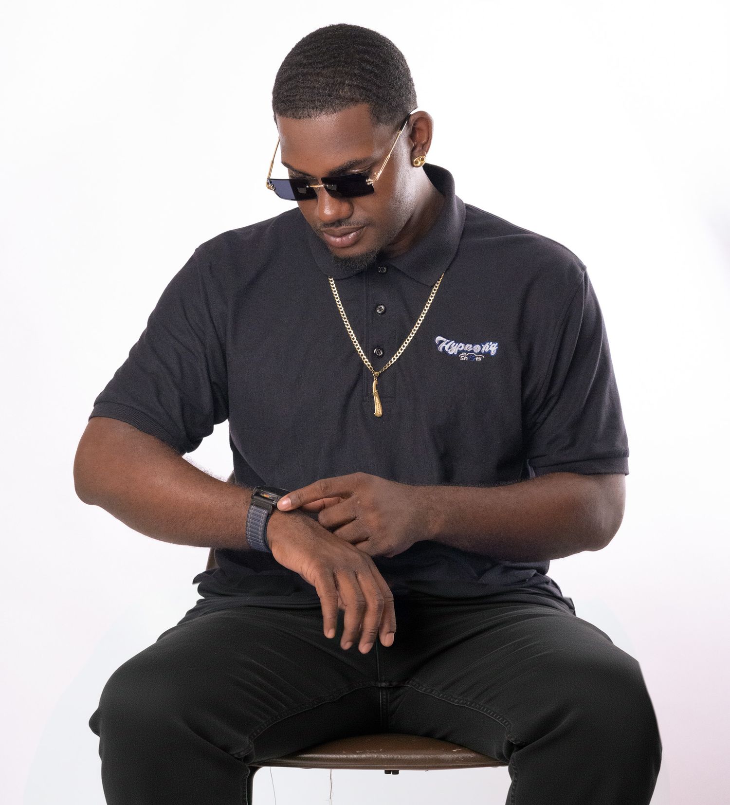 Person in black shirt and sunglasses sits casually while holding a mobile device.