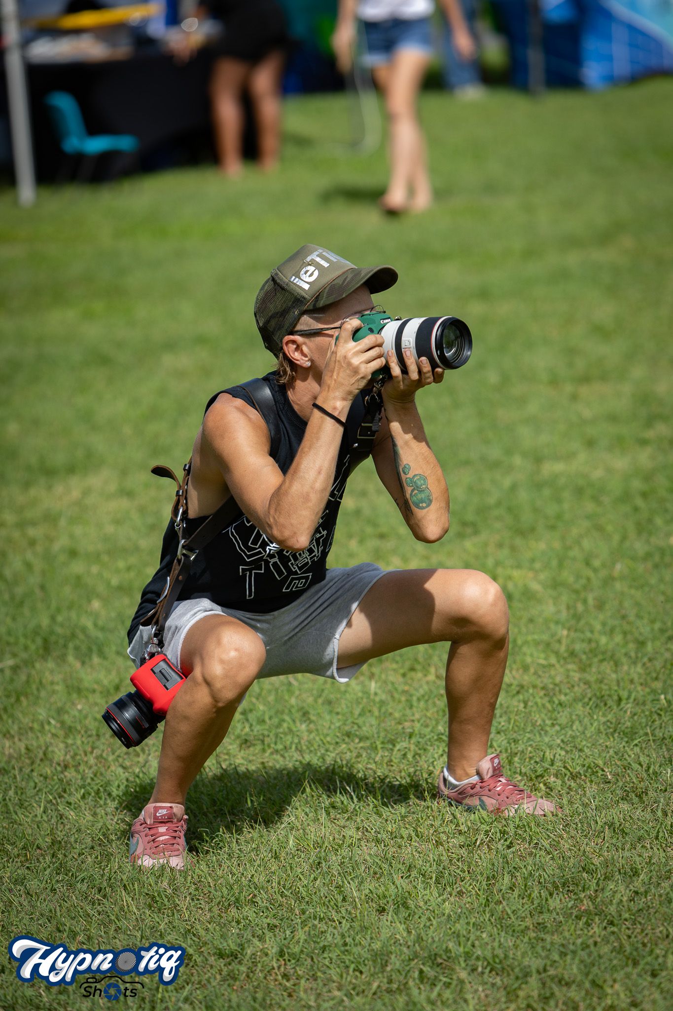 Photographer in athletic wear crouches low with camera to capture action shots on grass field.