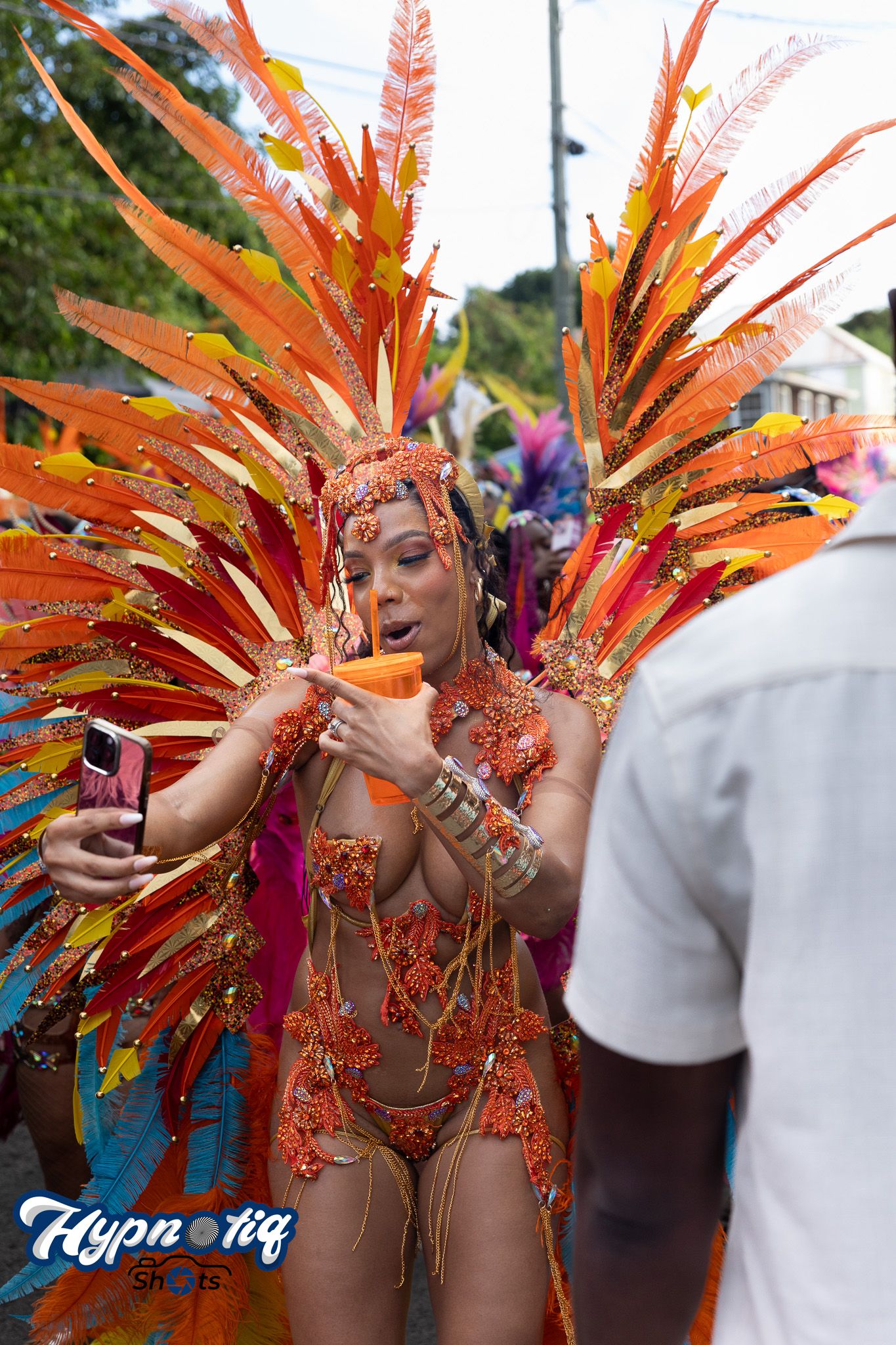 Dancer in vibrant orange and red feathered carnival costume performing at festival.
