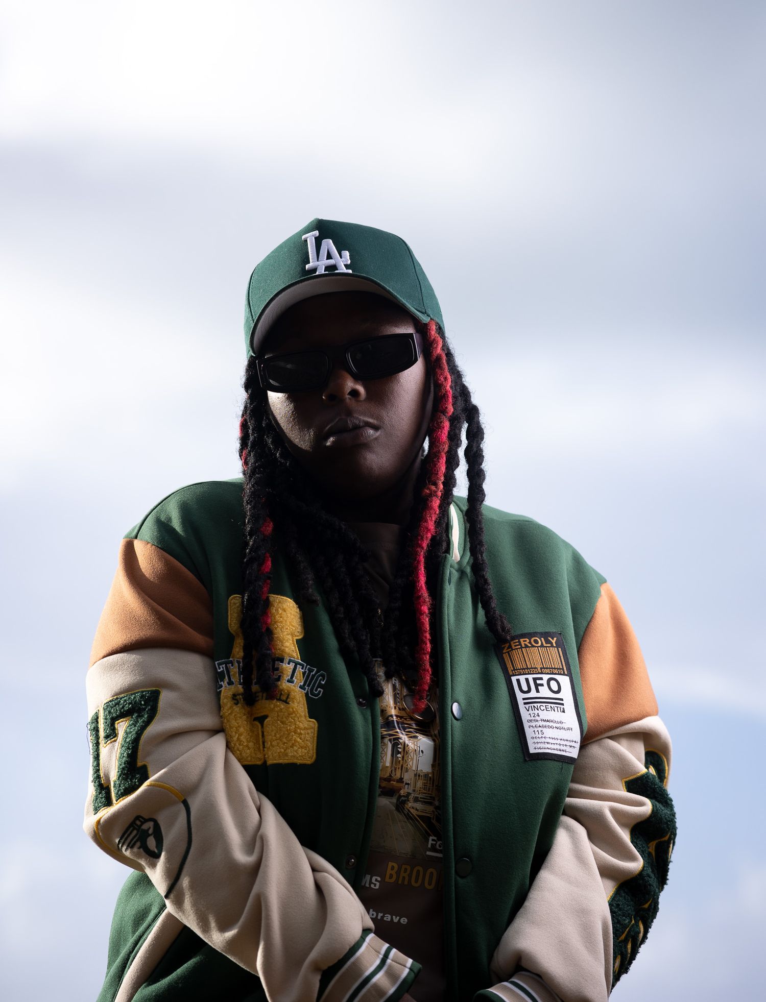 Fashion portraits in varsity jacket and baseball cap with braided hair accents.