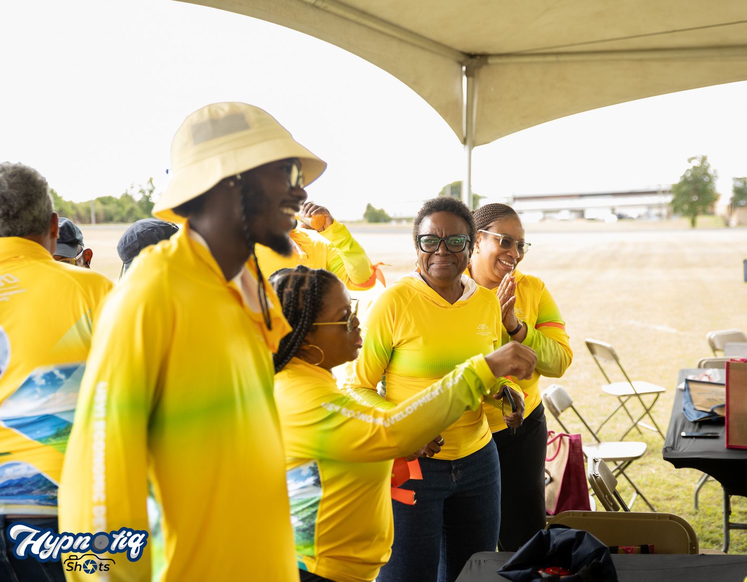 People in bright yellow uniforms gathered under a beige canopy.