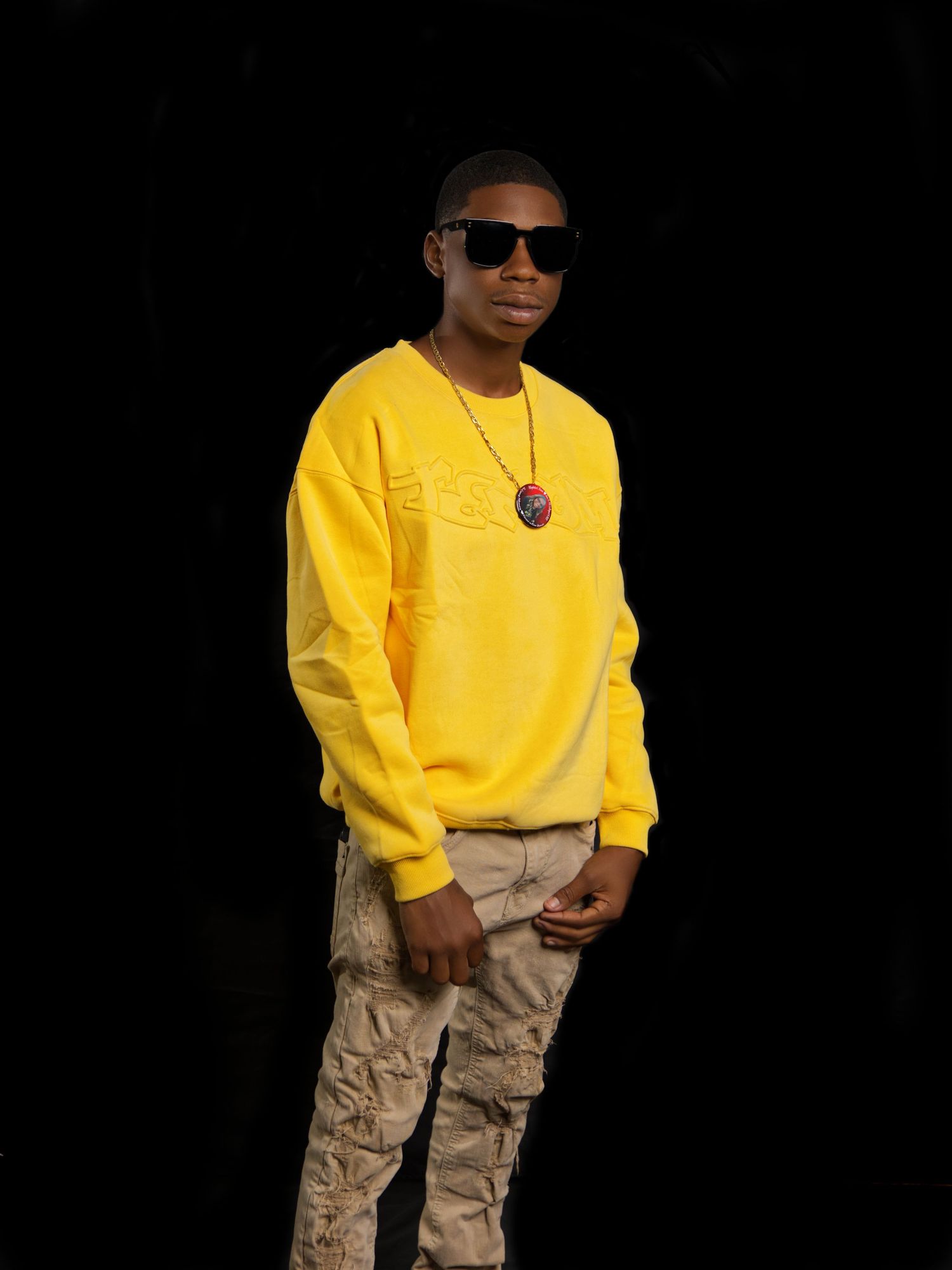 Person wearing yellow sweatshirt and cargo pants poses against dark background.
