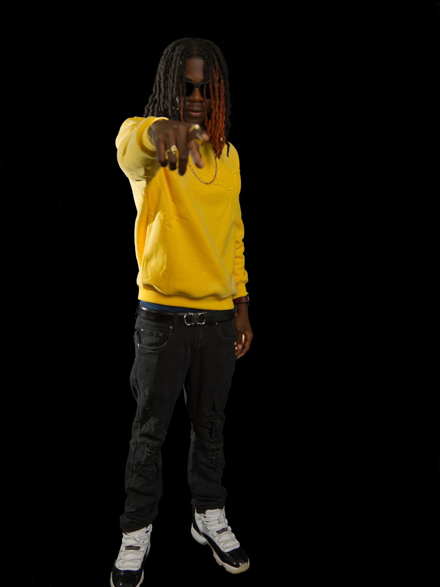 Urban fashion shoot featuring yellow sweater and dark pants against black background.