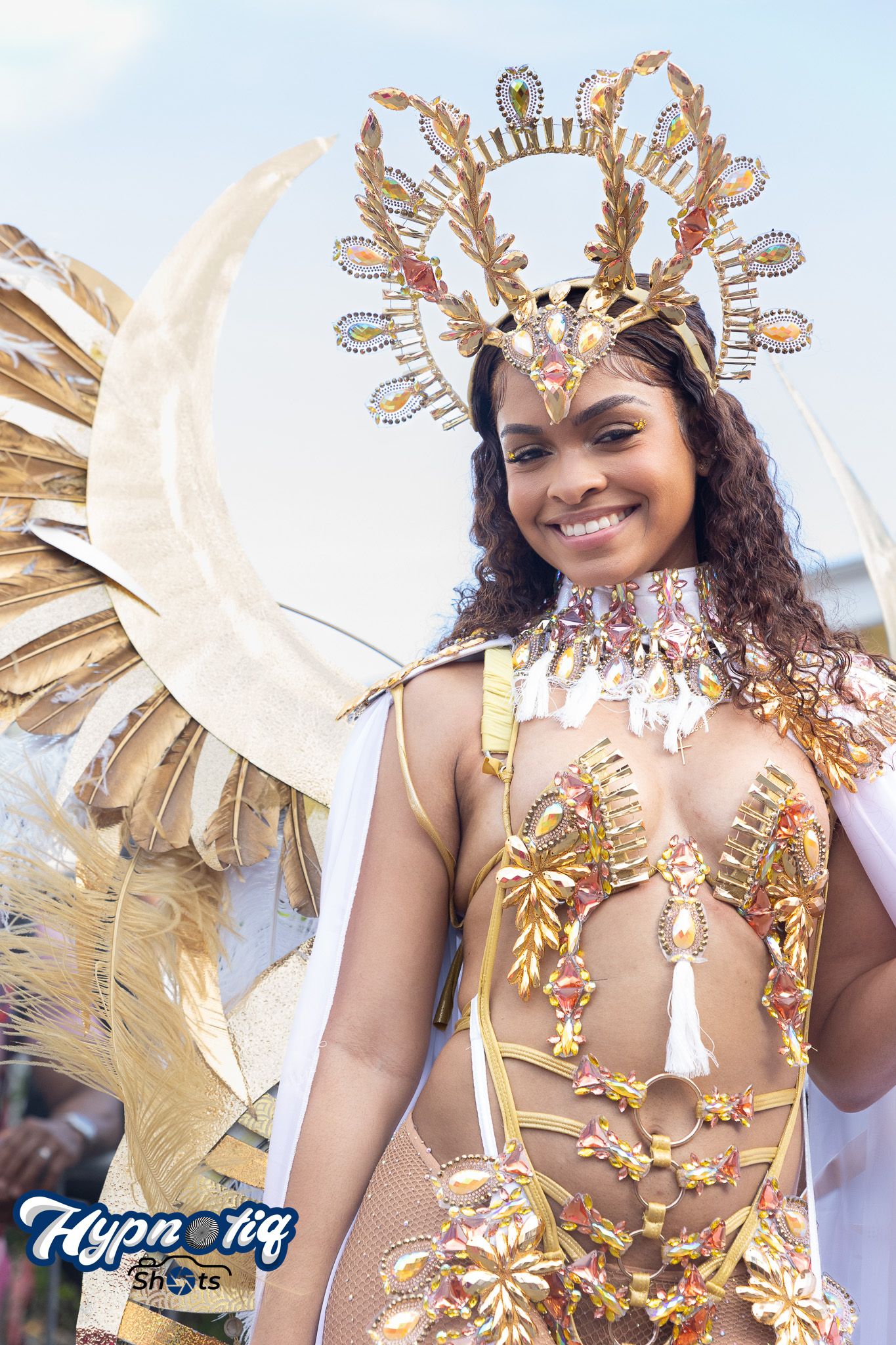 Carnival performer wearing elaborate gold and white feathered headdress and costume.