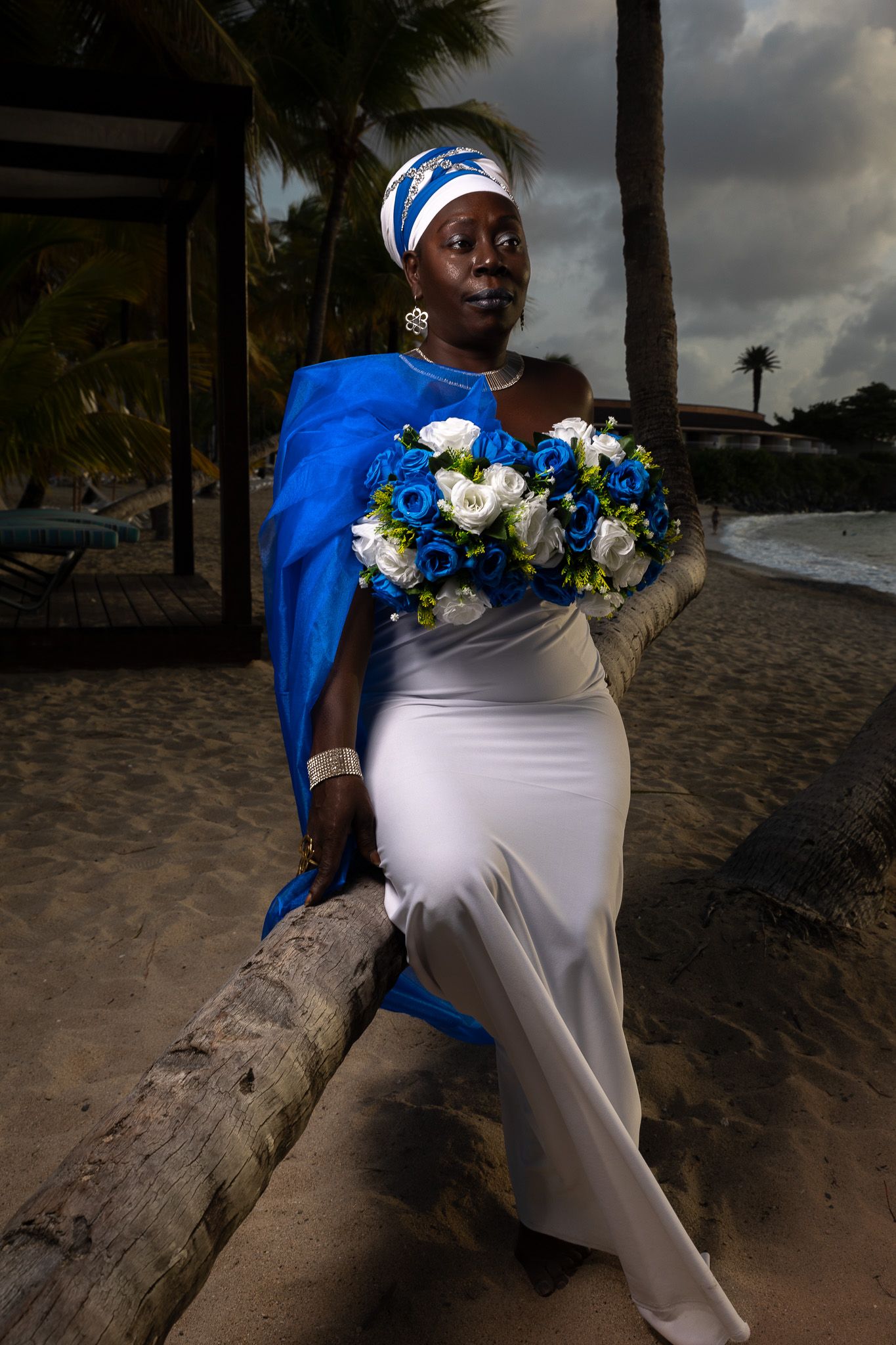 Beach portrait series with white dress and blue cape against palm trees and sand.