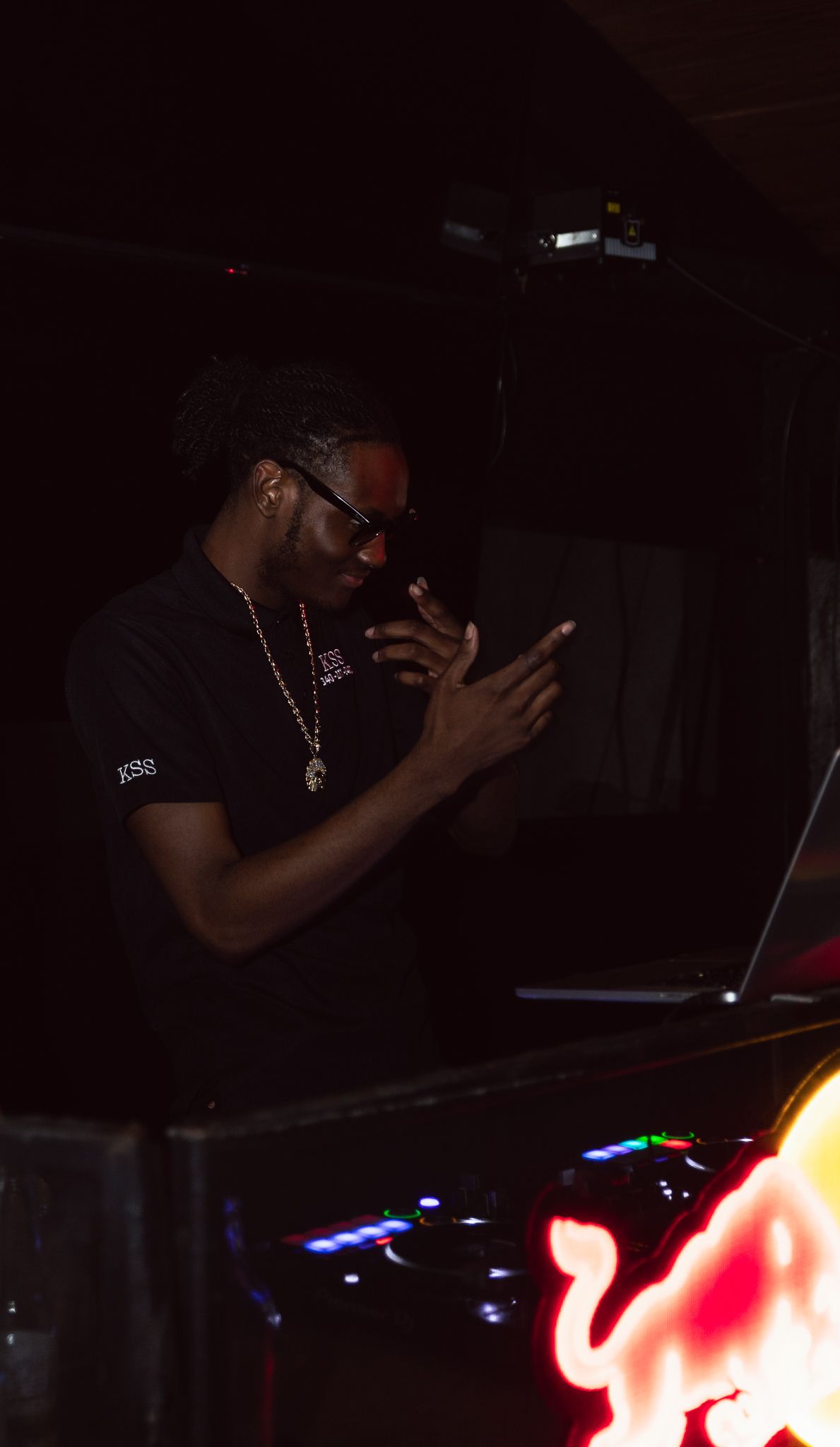DJ performing at nightclub with illuminated equipment in dark setting.