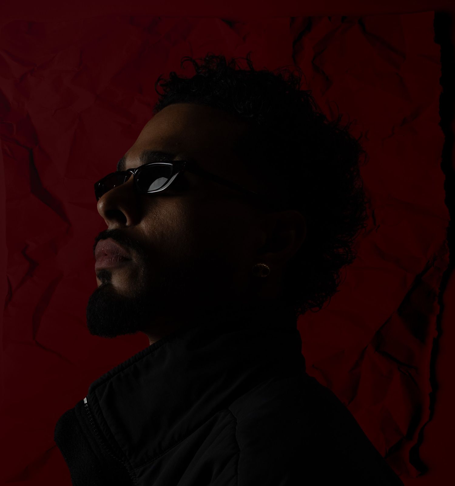 Silhouetted profile against deep red background in dramatic lighting.