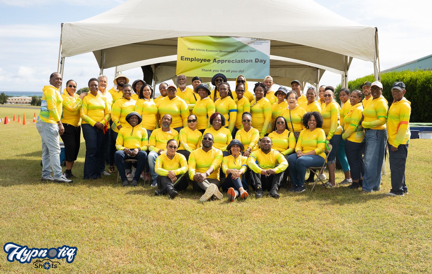 Large group wearing yellow shirts gathered under white tent at outdoor event.