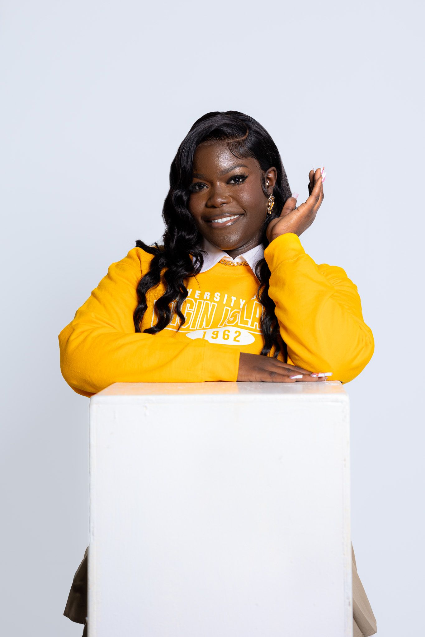 Studio portrait with someone in a bright yellow sweater posing with a white cube prop.