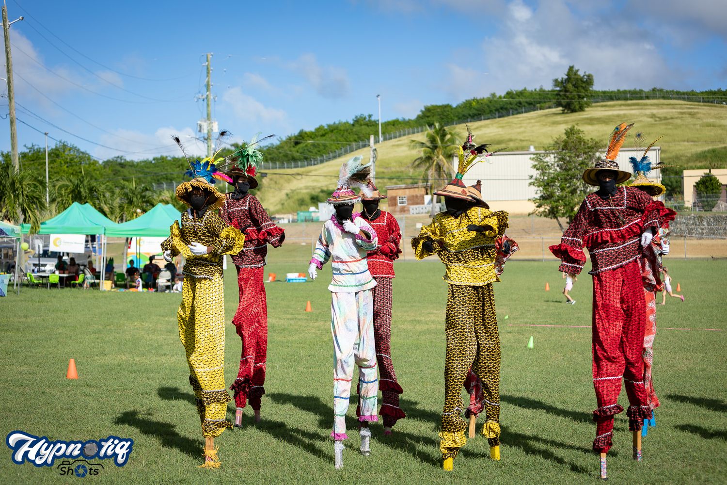 People in colorful costumes perform in line formation on sunny outdoor field.