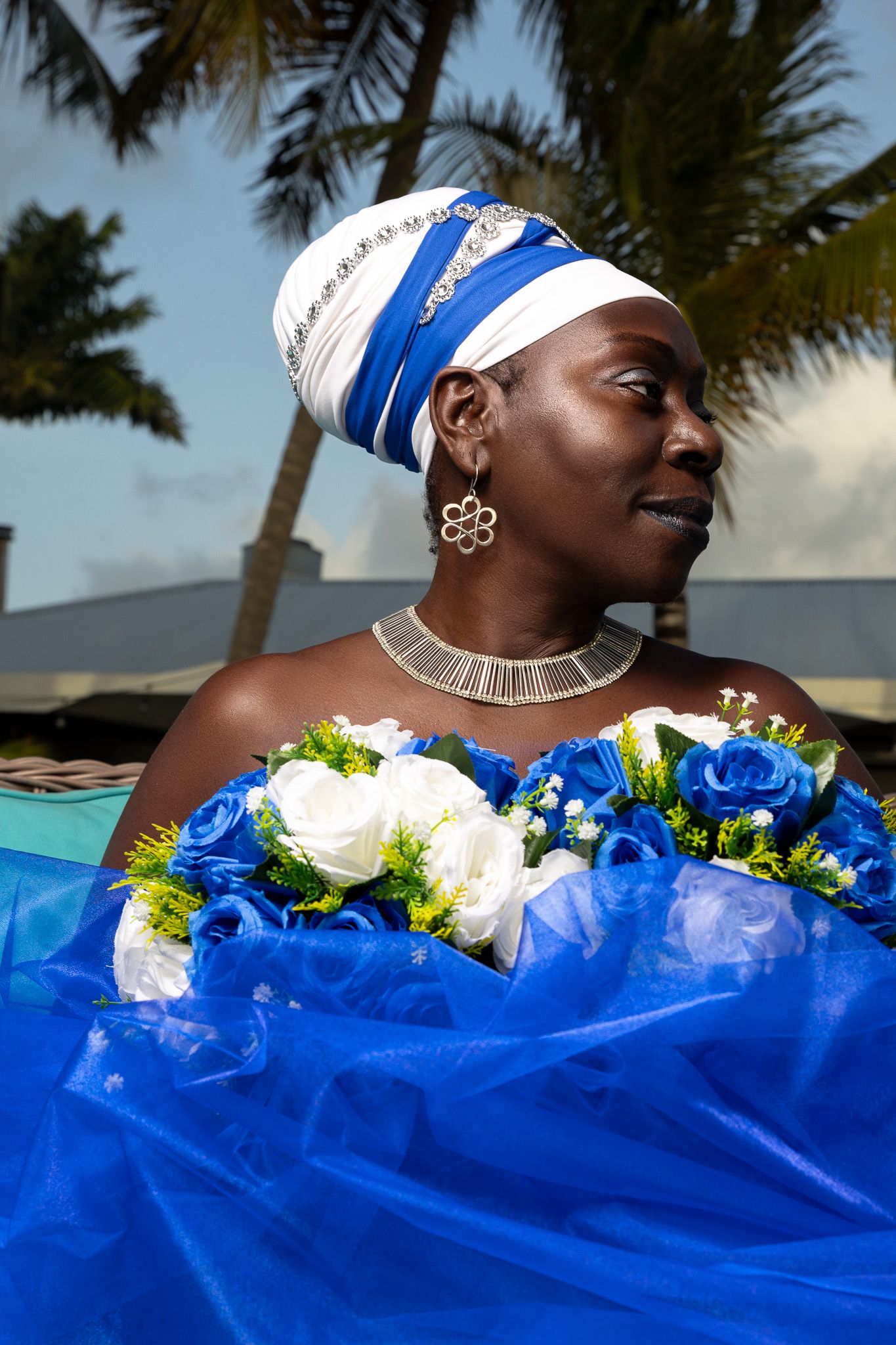 Artistic beach photoshoot featuring blue fabric and white floral arrangements with palm trees in background.