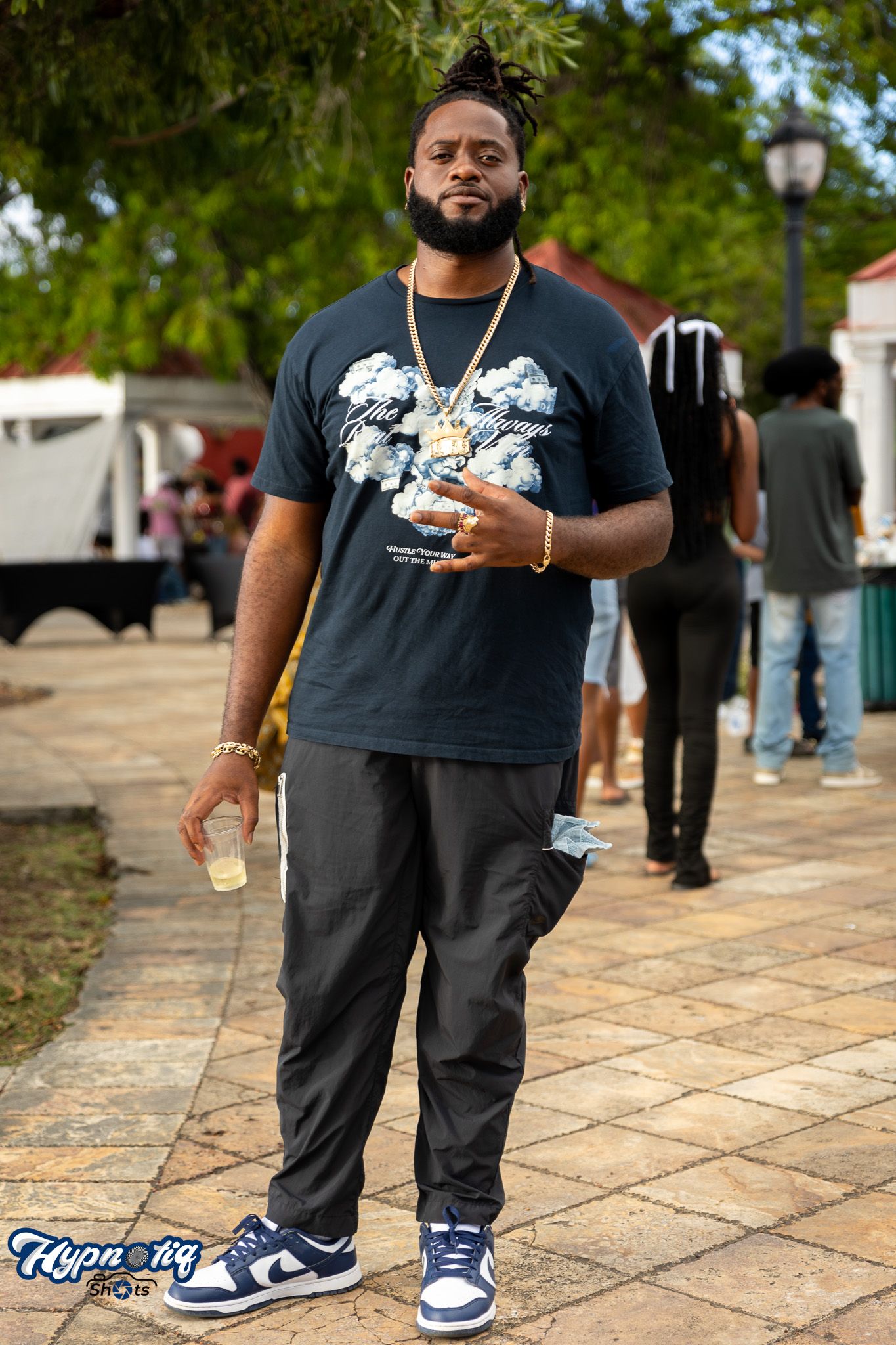 Street fashion series showing black graphic t-shirt and blue sneakers on stone pavement.