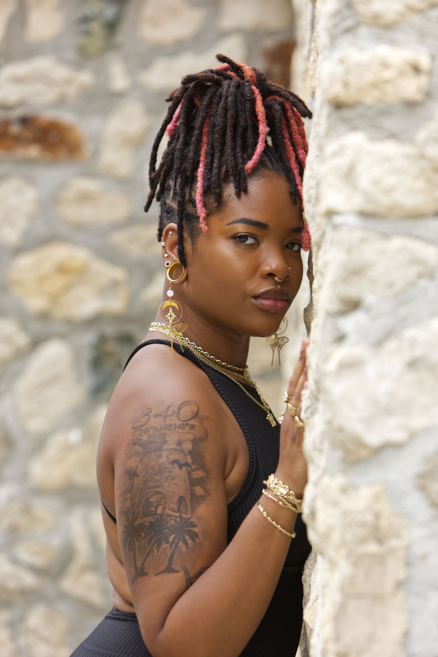 Artistic portraits against stone wall showing tattoo art and jewelry details.
