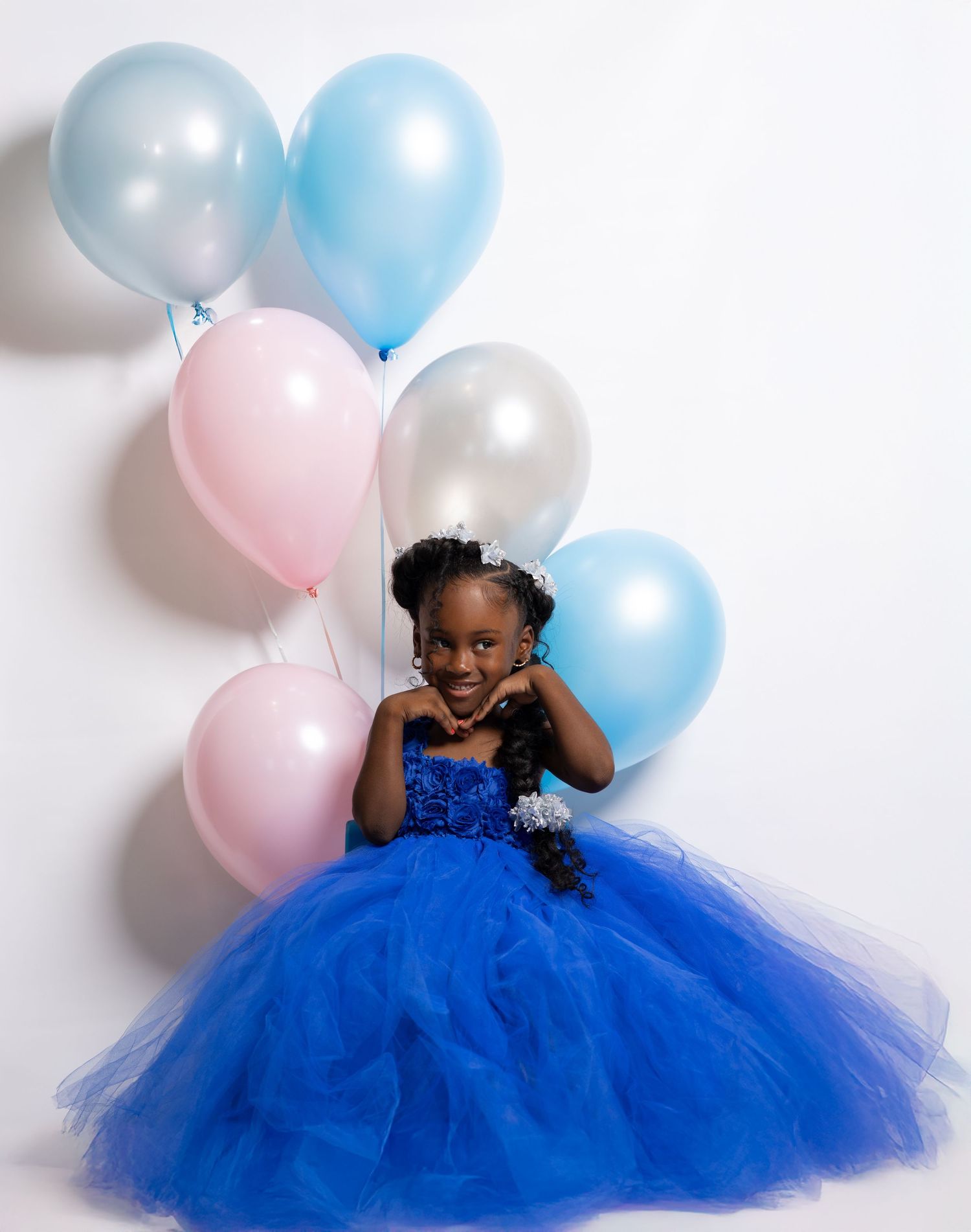 Child in a royal blue tulle dress poses with pink and blue balloons against a white backdrop.