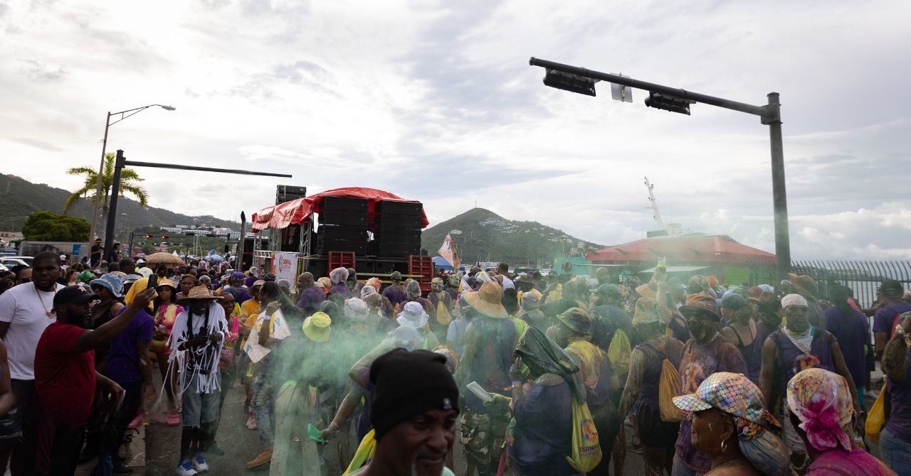 Crowded outdoor festival scene with mountains visible in the background under cloudy skies.