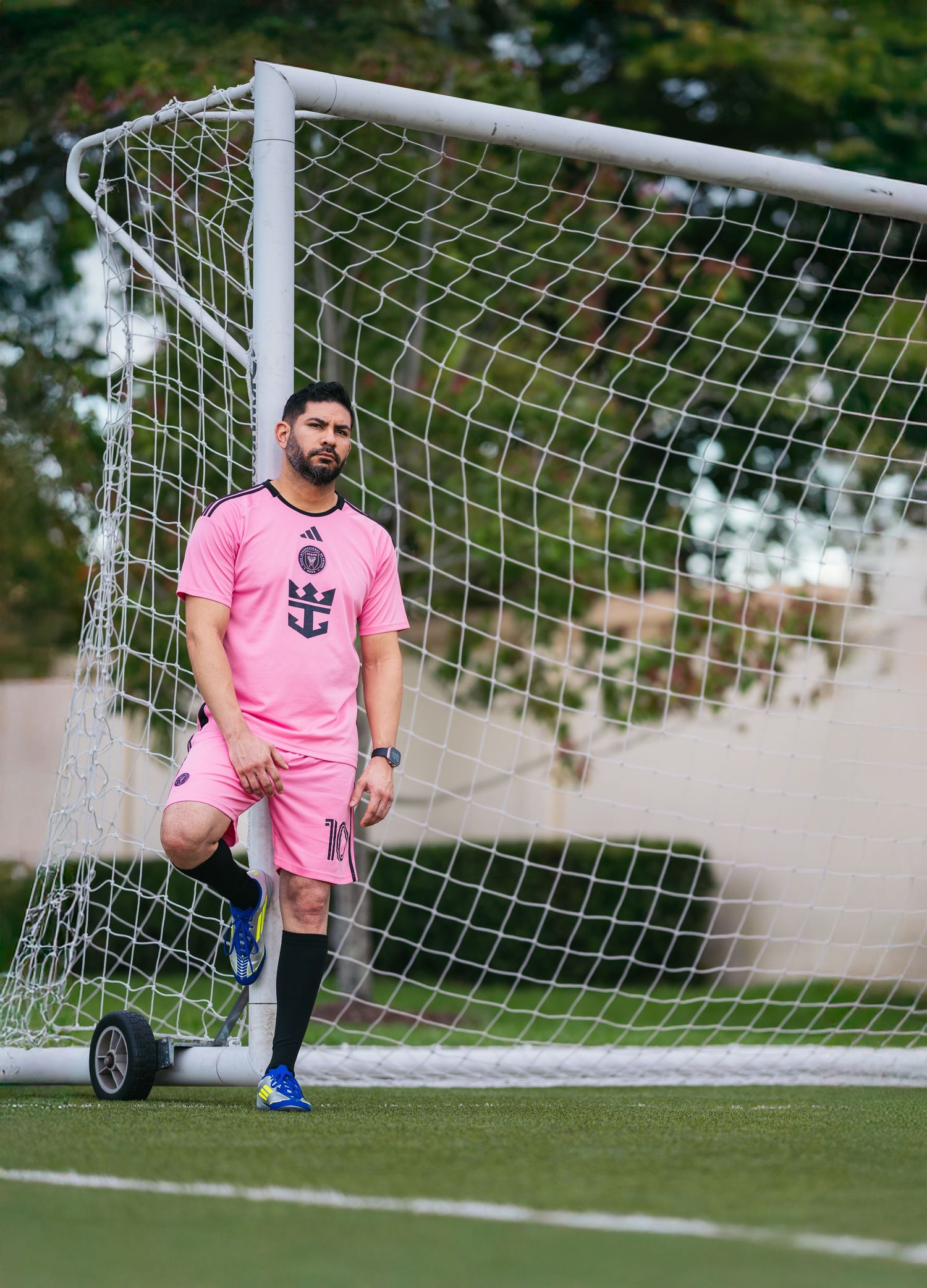 A man in pink soccer uniform standing by the goal on a sports field.