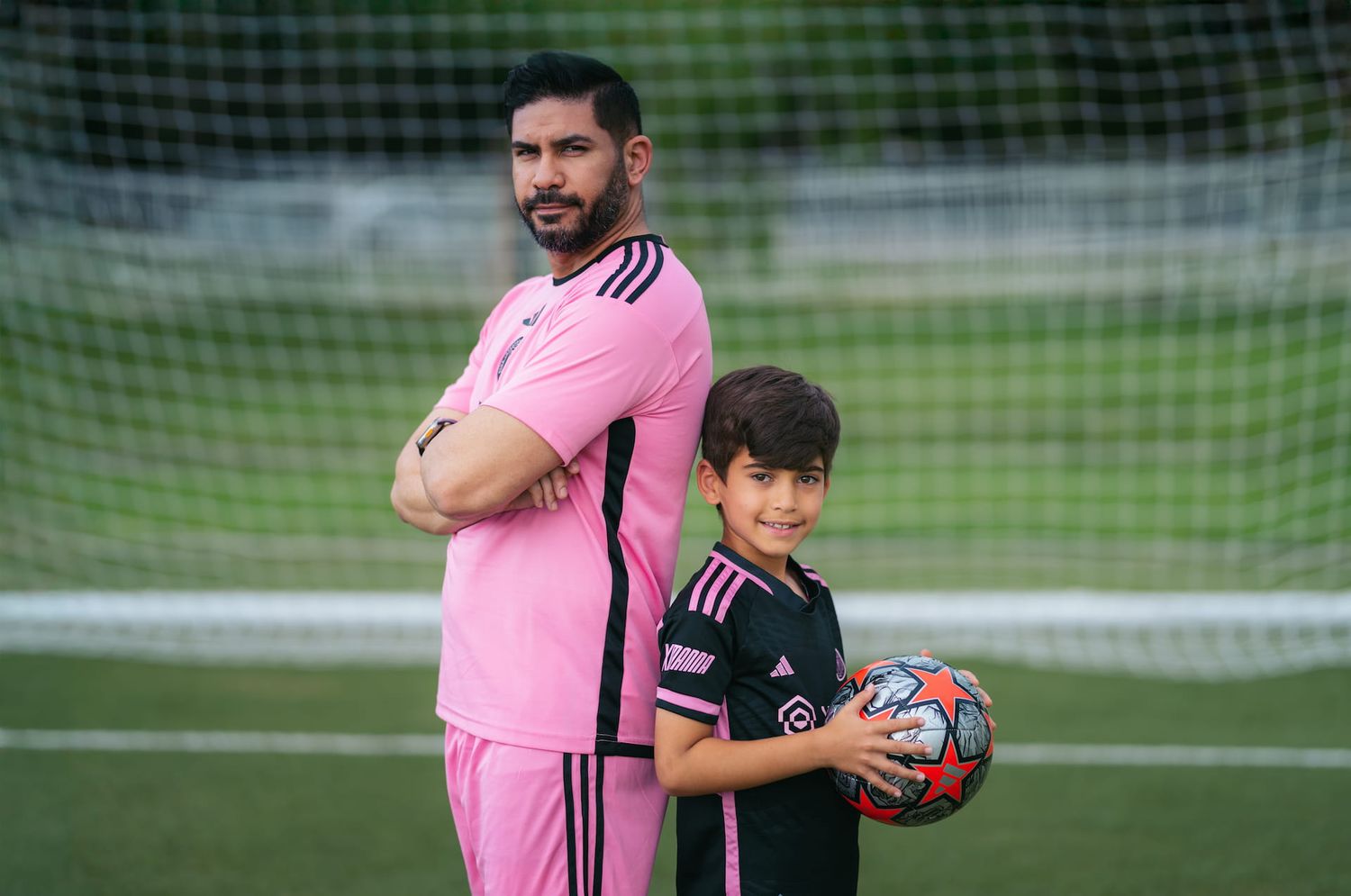 Soccer players in pink and dark uniforms interact on a field with goal nets visible.