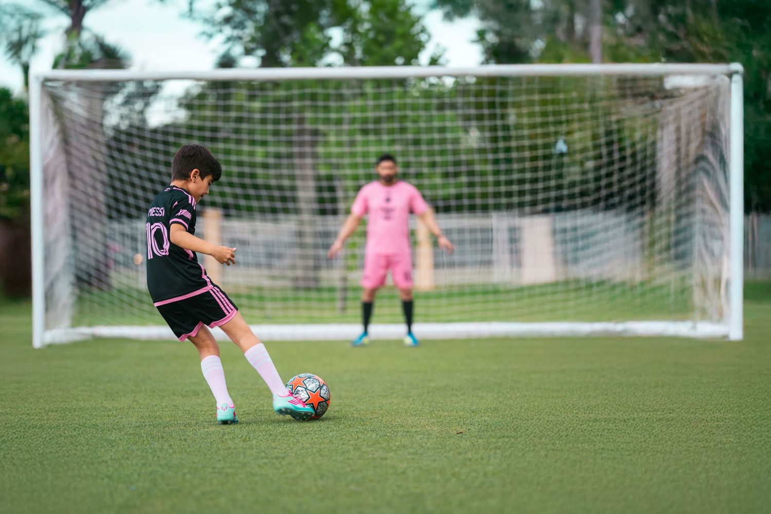 Young soccer player taking a penalty kick on a green field with a goalkeeper defending the goal.
