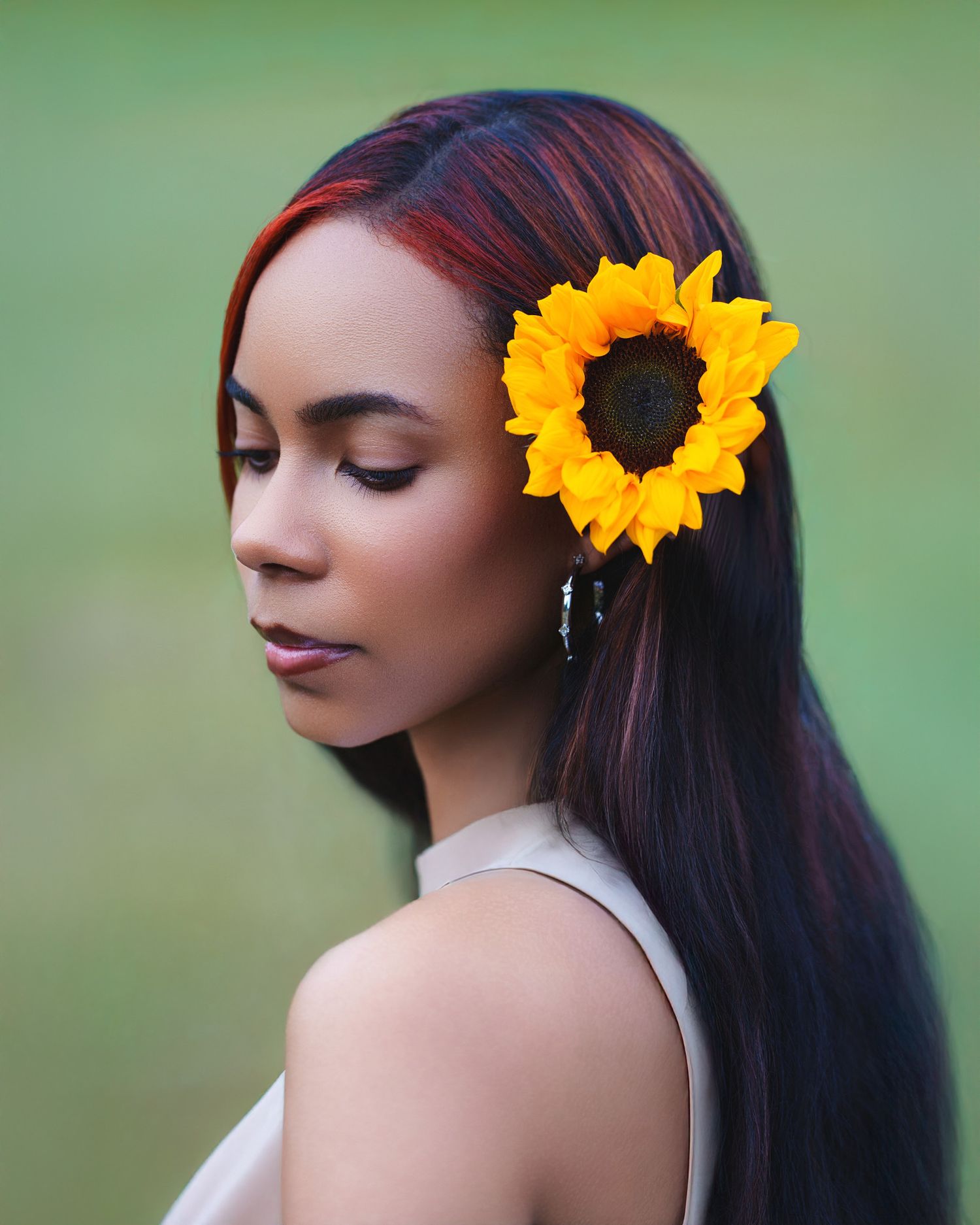 Portrait of a woman with yellow sunflowers in her hair against a soft green background.