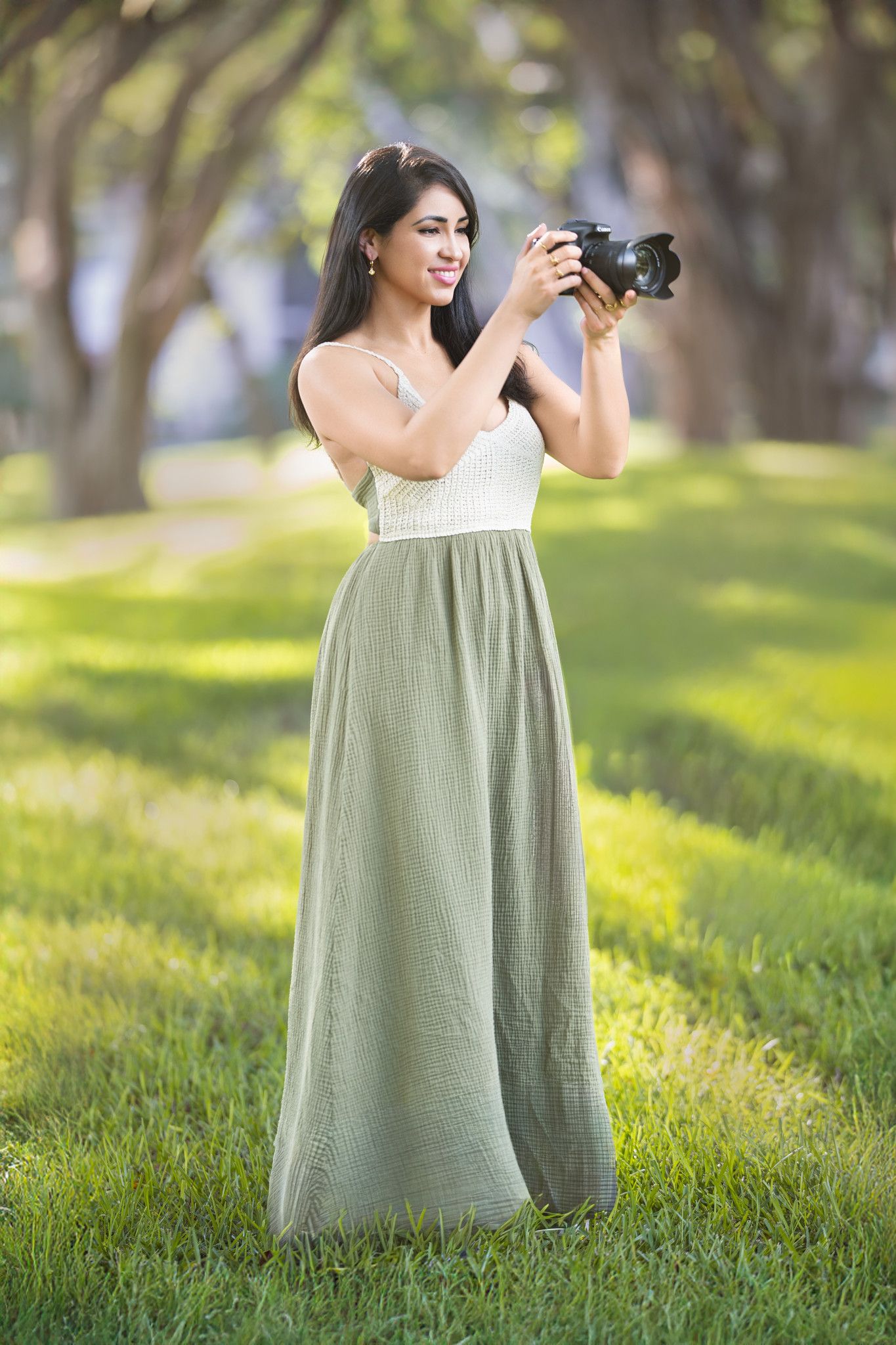 person wearing a flowing sage green dress standing on sunlit grass.