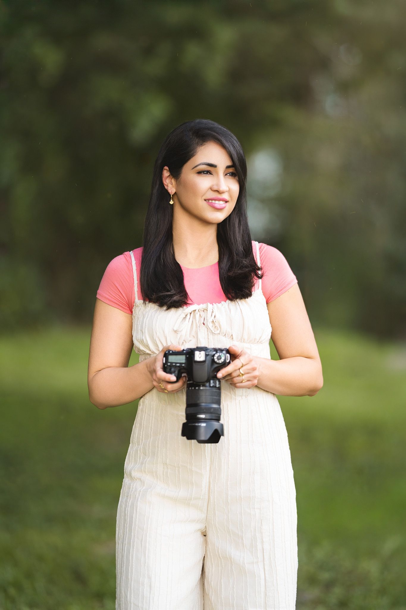 Photographer in beige overalls holding a camera in a sunny outdoor setting.