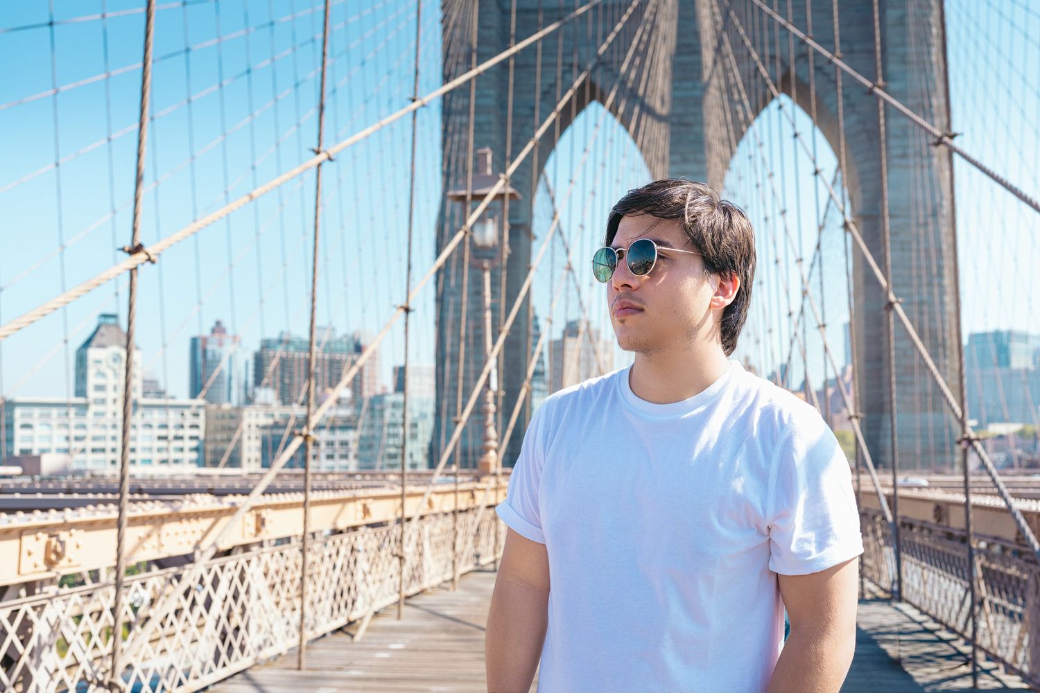 A group of people walking and taking photos on the Brooklyn Bridge with Manhattan skyline in the background.