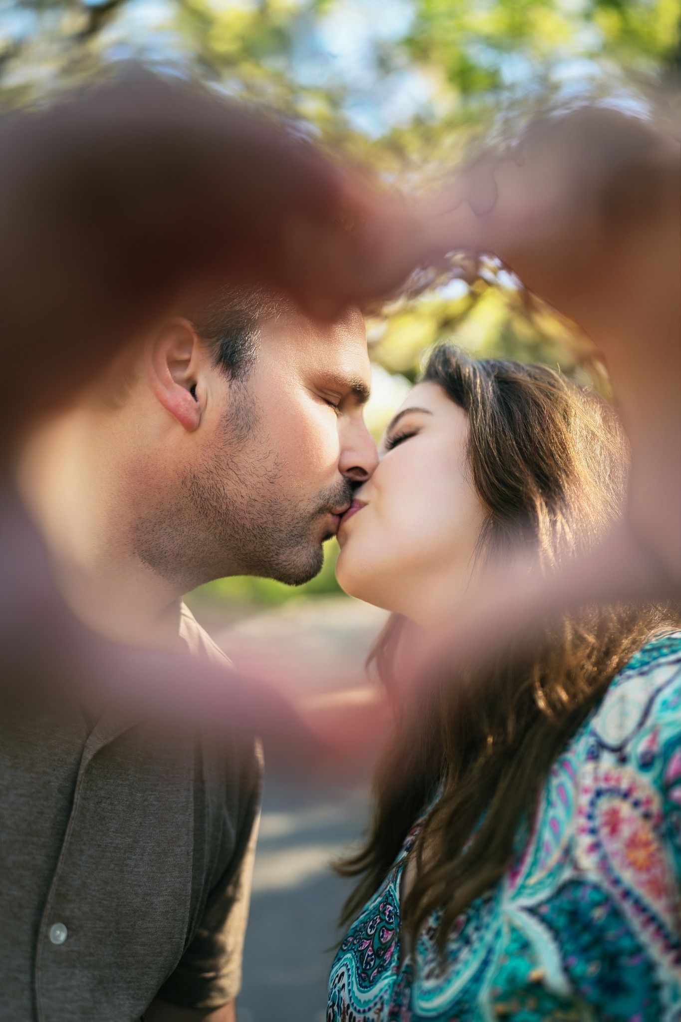Romantic couple sharing a tender kiss outdoors, framed by a blurred heart shape in soft focus.