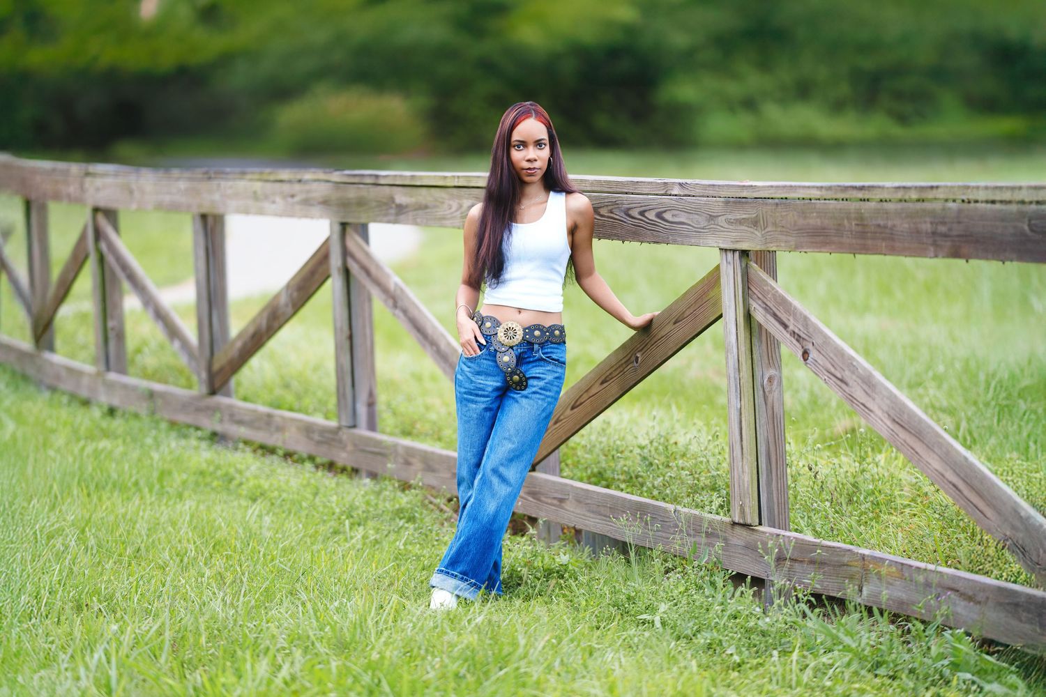 A rustic wooden fence stretches across a lush green field on a bright summer day.