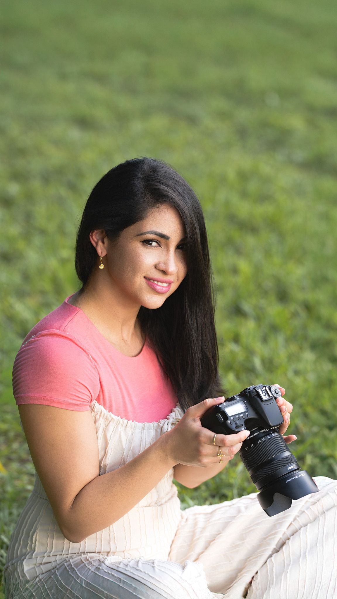 Portrait of a woman sitting on grass while holding a camera.