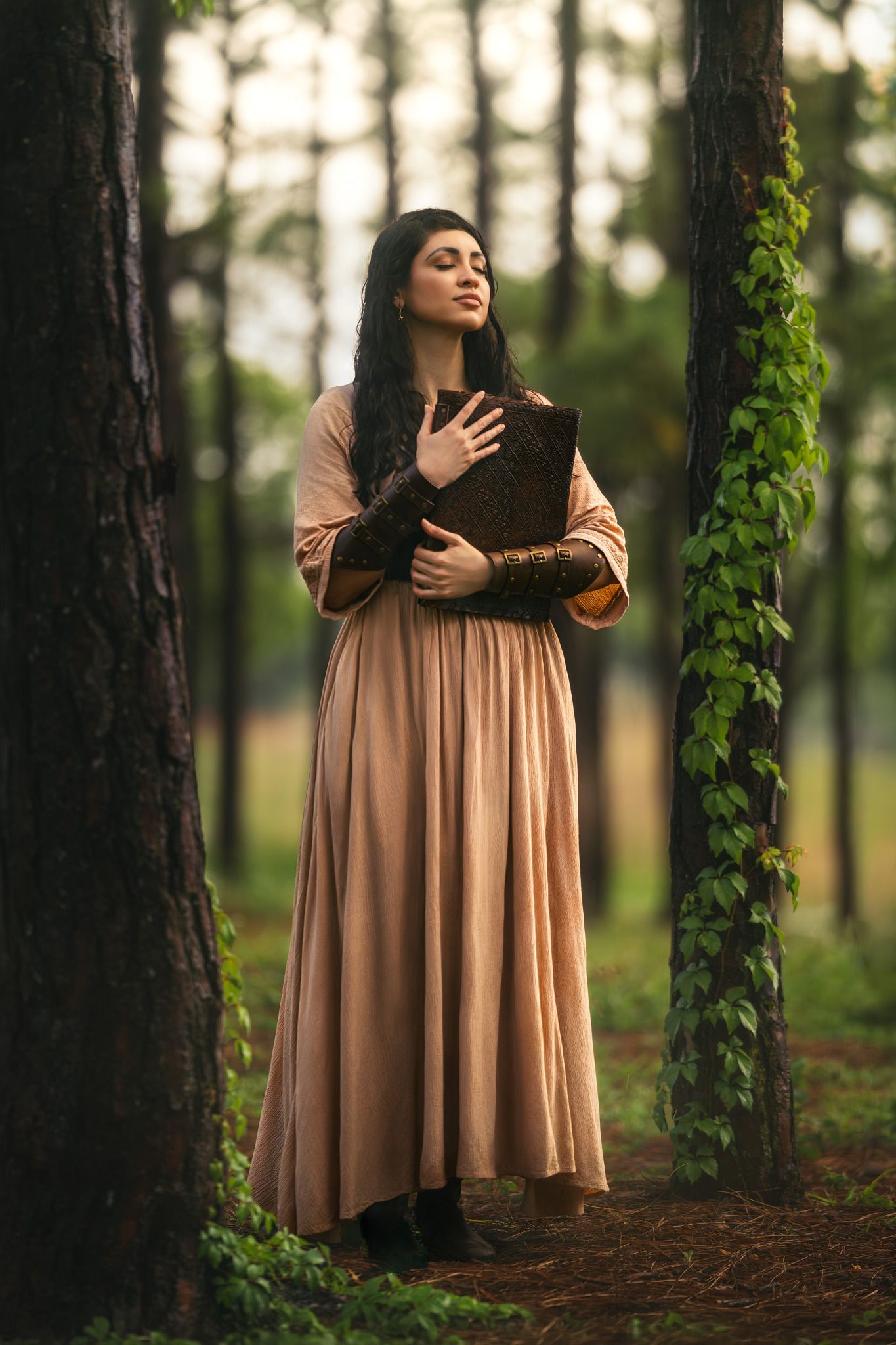 Woman in beige medieval gown holding ancient book in misty forest setting.