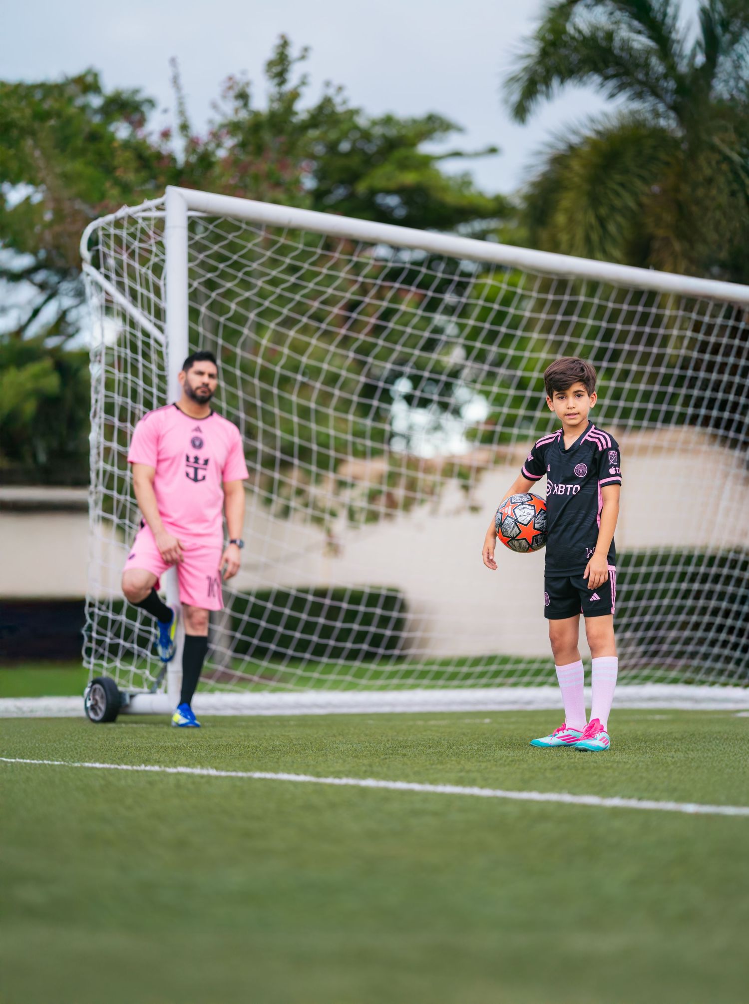 Two soccer players in Inter Miami CF uniforms stand near a goal on a green turf field, one holding a ball.
