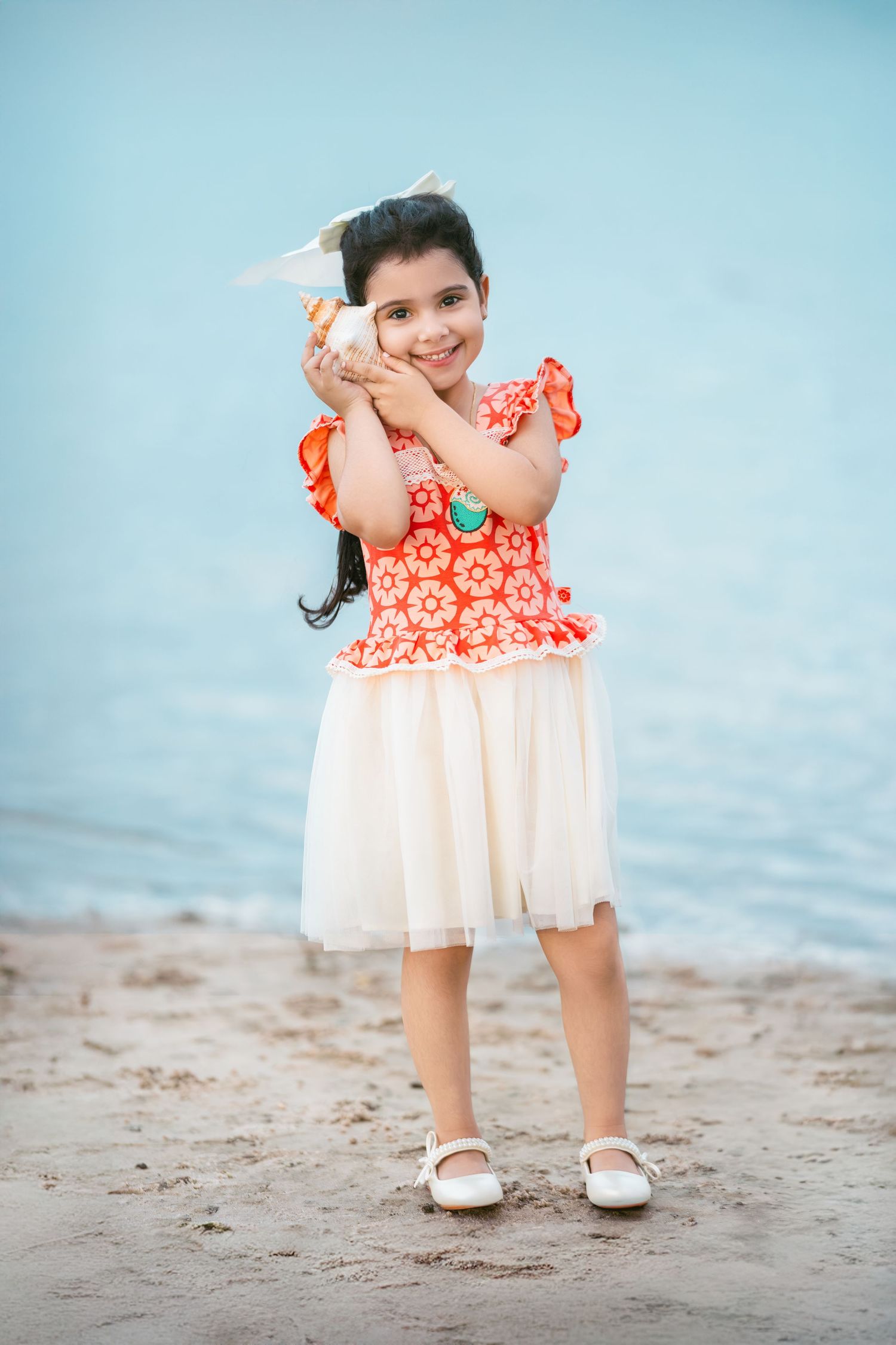 A child in a red and white dress plays on the beach, showing different playful poses against a blue sky background.
