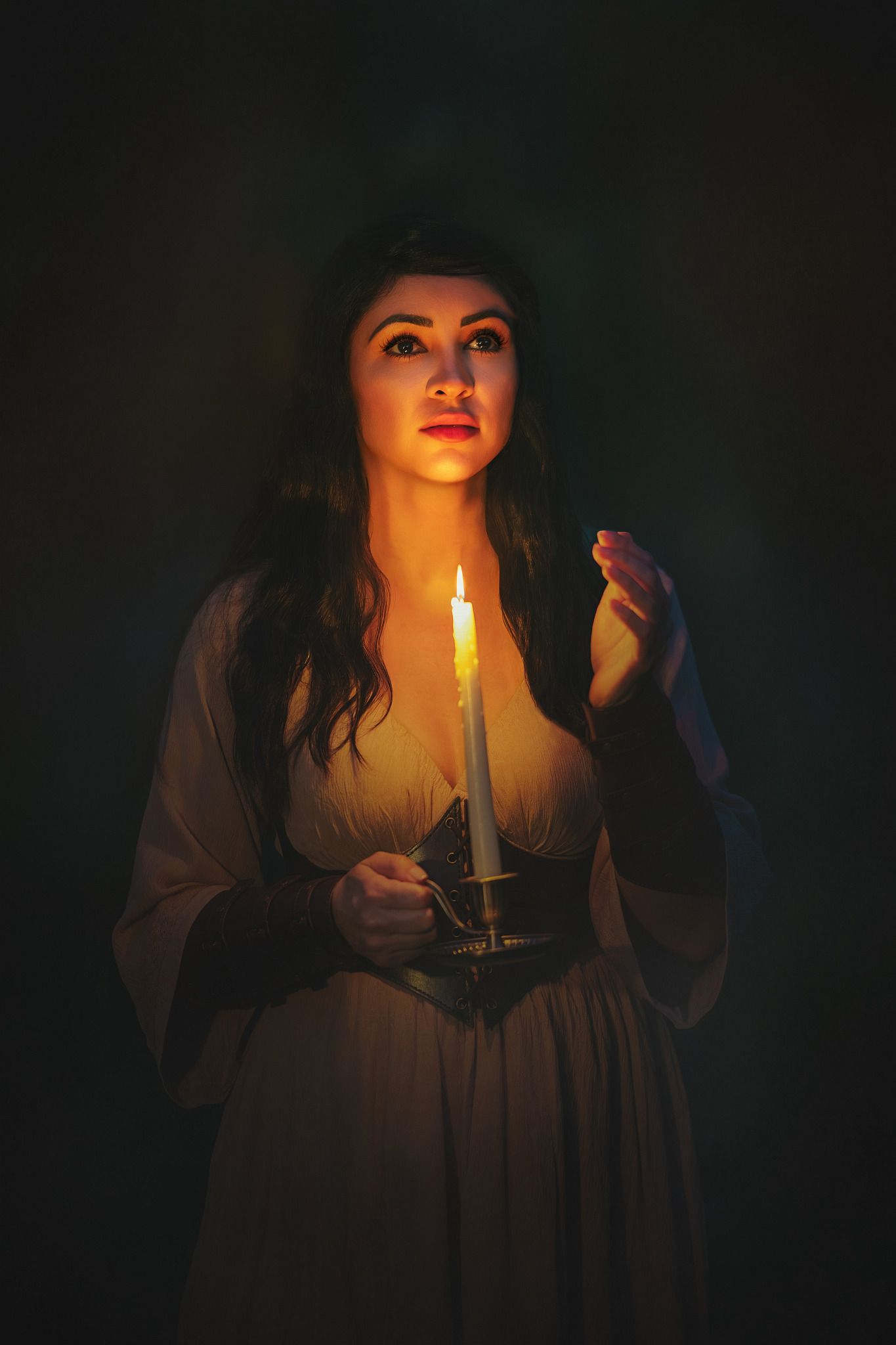 Woman in vintage dress holding a glowing candle in dark, moody atmospheric portrait photography.