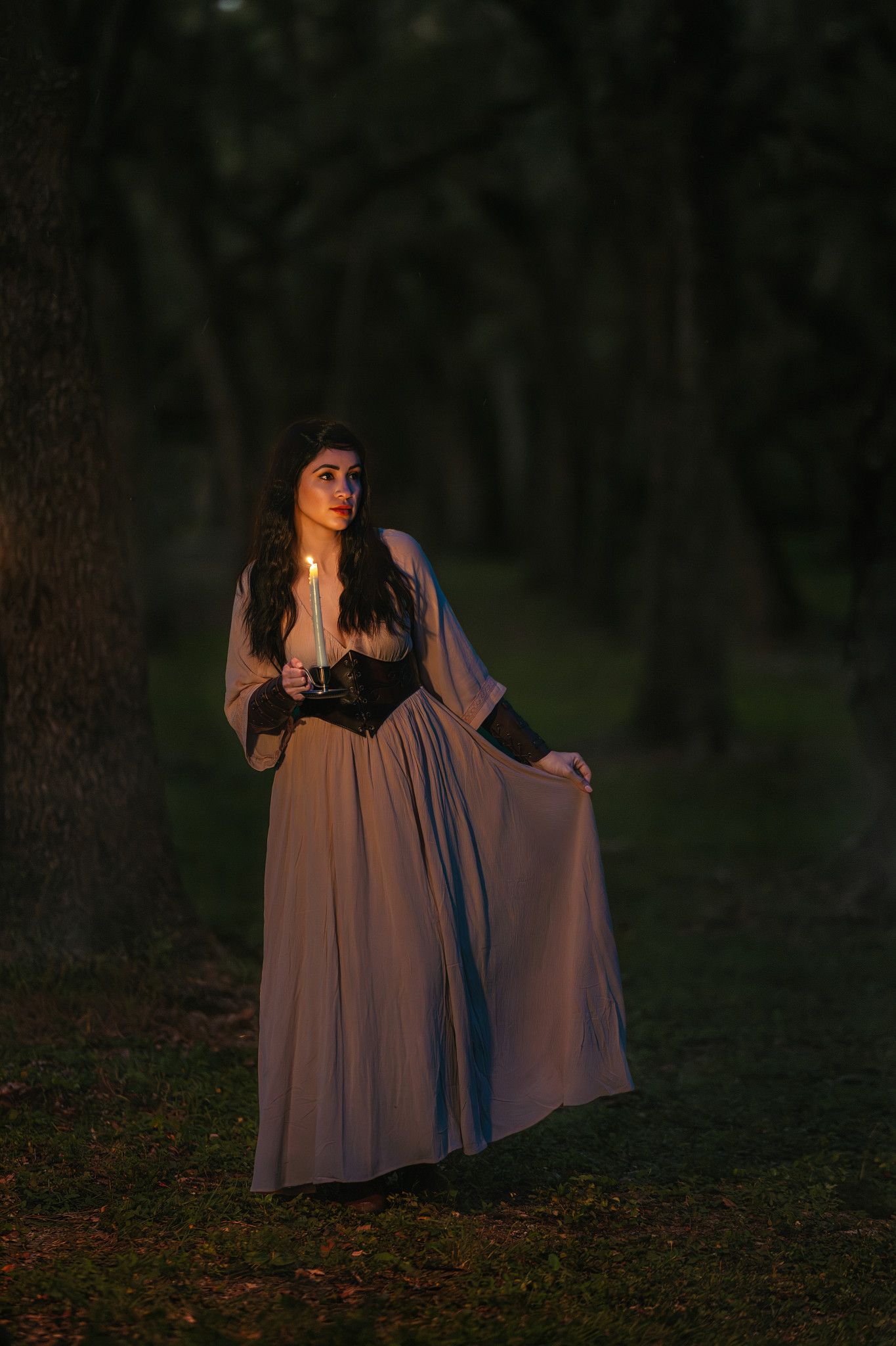 A flowing mauve dress catches the evening light in a moody forest setting during a dramatic outdoor photoshoot.