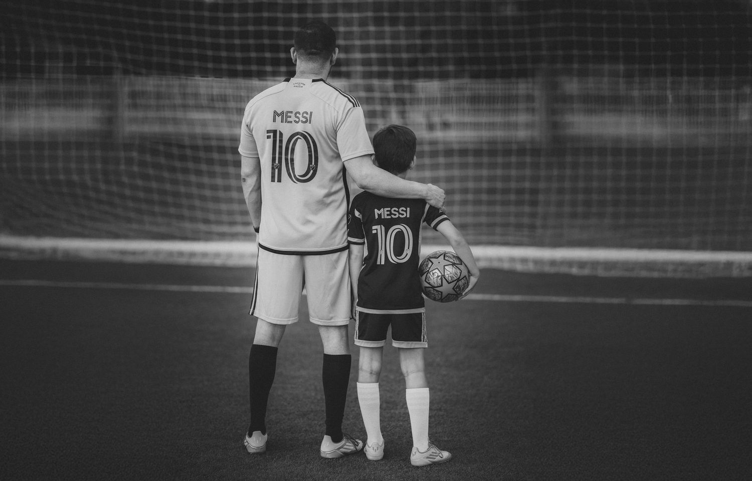 Black and white photo of two people wearing Messi number 10 jerseys standing together on a soccer field.