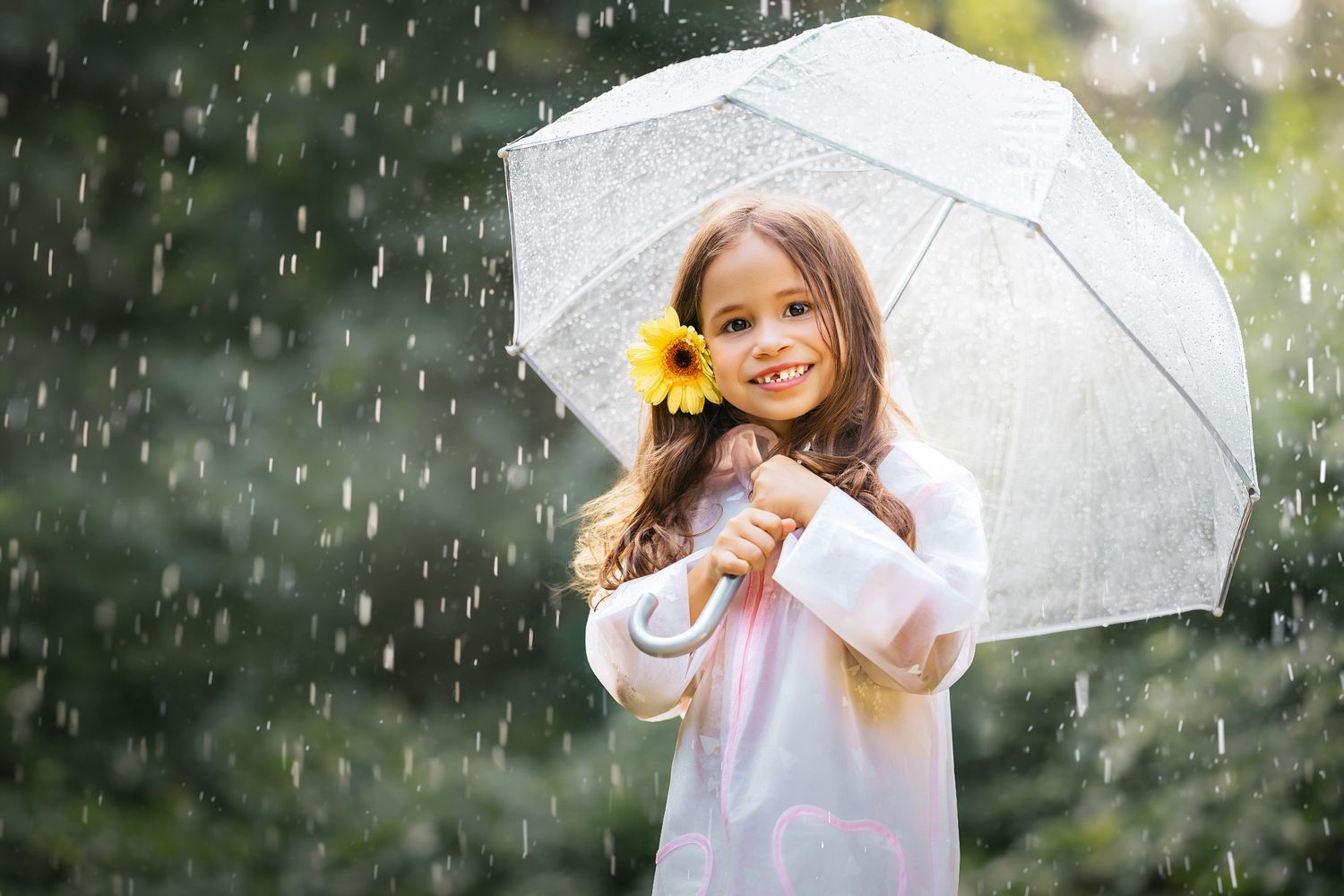 Smiling girl in white raincoat holding lace umbrella and sunflower in the rain outdoors.