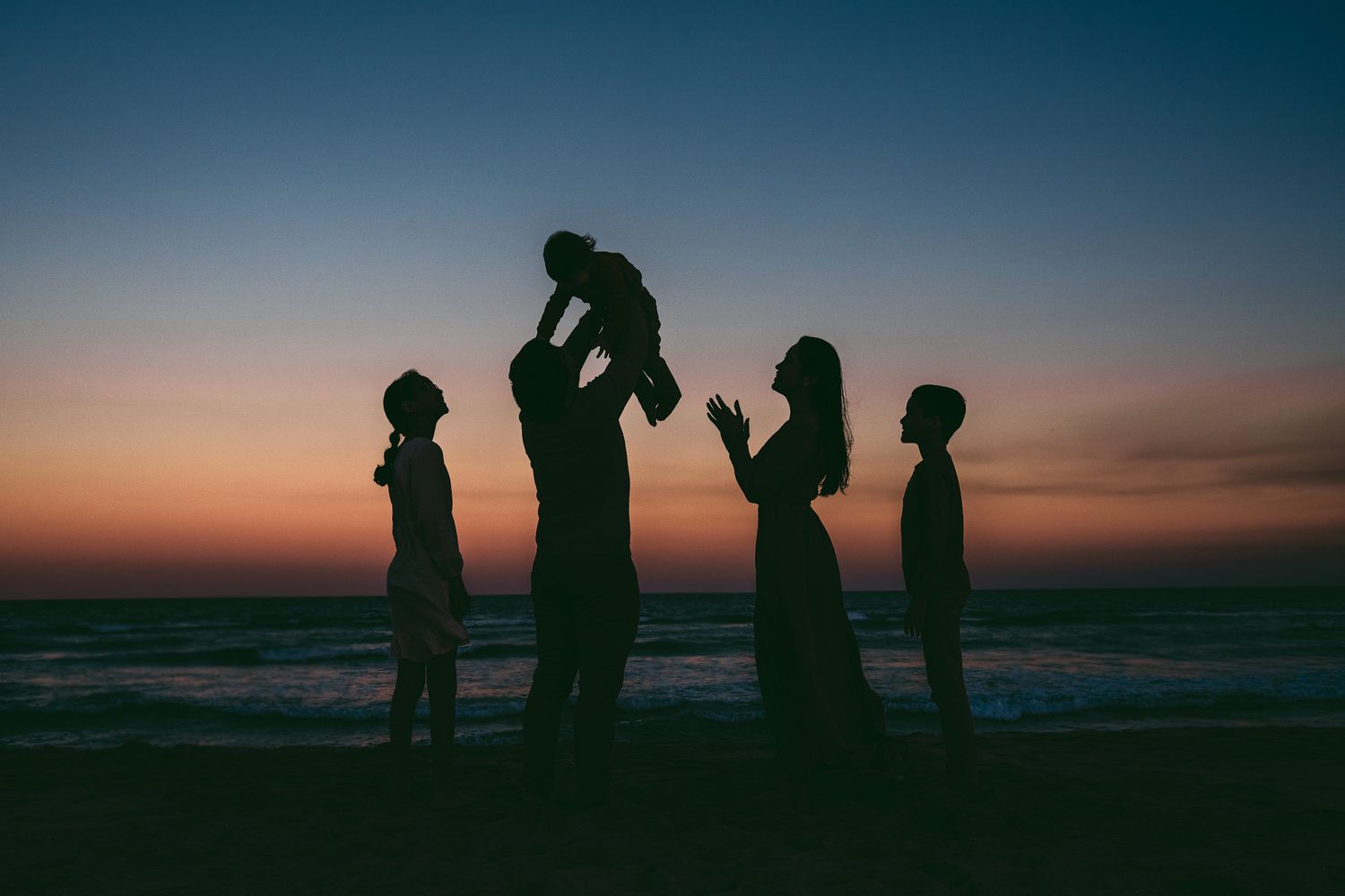 Silhouettes of people standing together against a dramatic sunset sky at the beach.