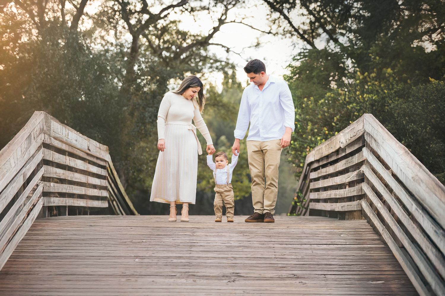 A couple walks together on a wooden boardwalk through a natural outdoor setting during golden hour.