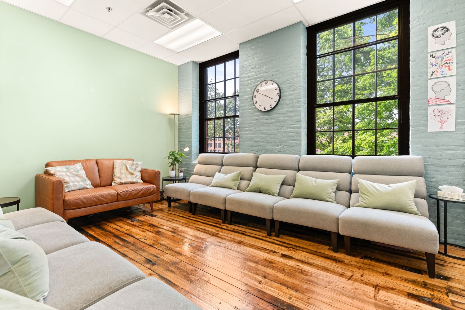 Modern lounge with mint green walls, hardwood floors, and mix of tan and grey seating.