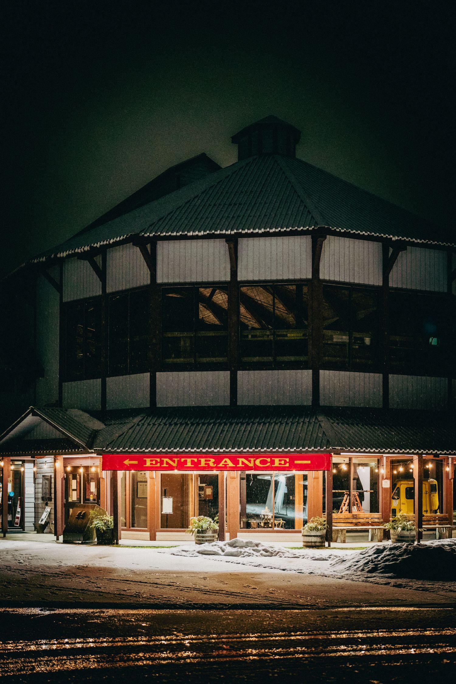 Illuminated strip mall storefronts at night with snow covered ground and dark moody atmosphere.