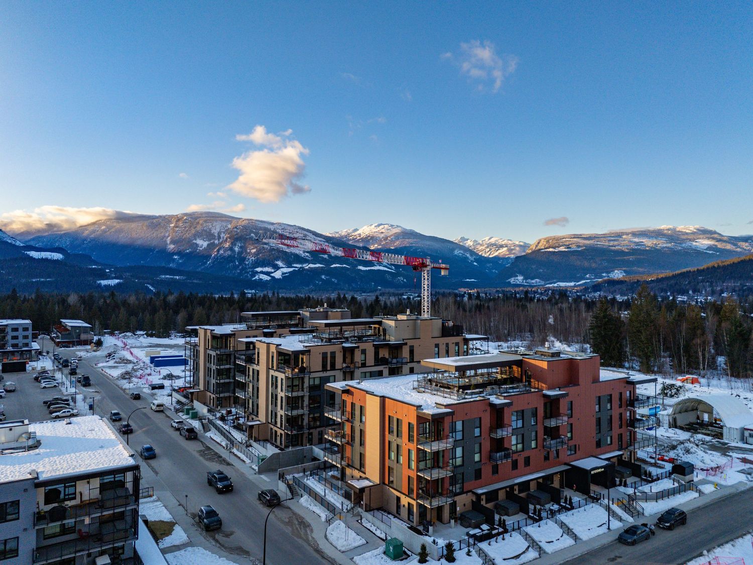 Panoramic winter view of a mountain town with snow-covered buildings and peaks against a clear blue sky.
