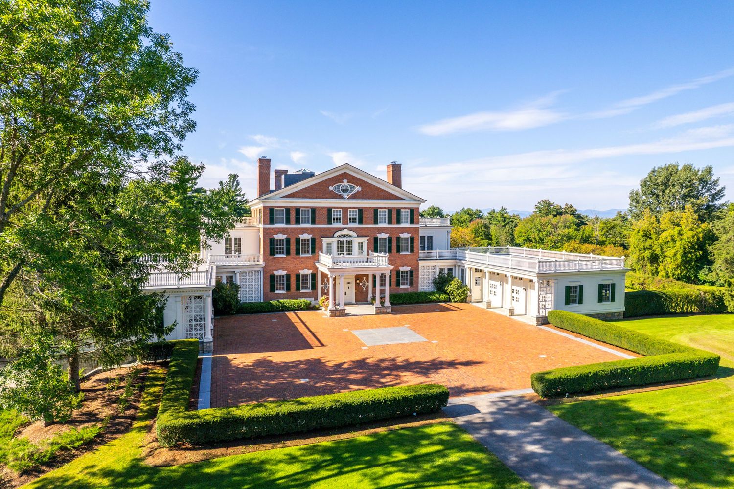 Aerial view of a grand estate with circular driveway and manicured lawns on a sunny day.