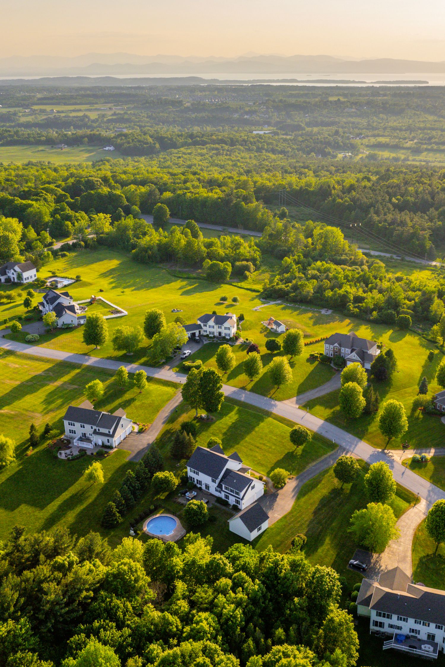 Drone view of luxury homes with pools scattered across lush green countryside.