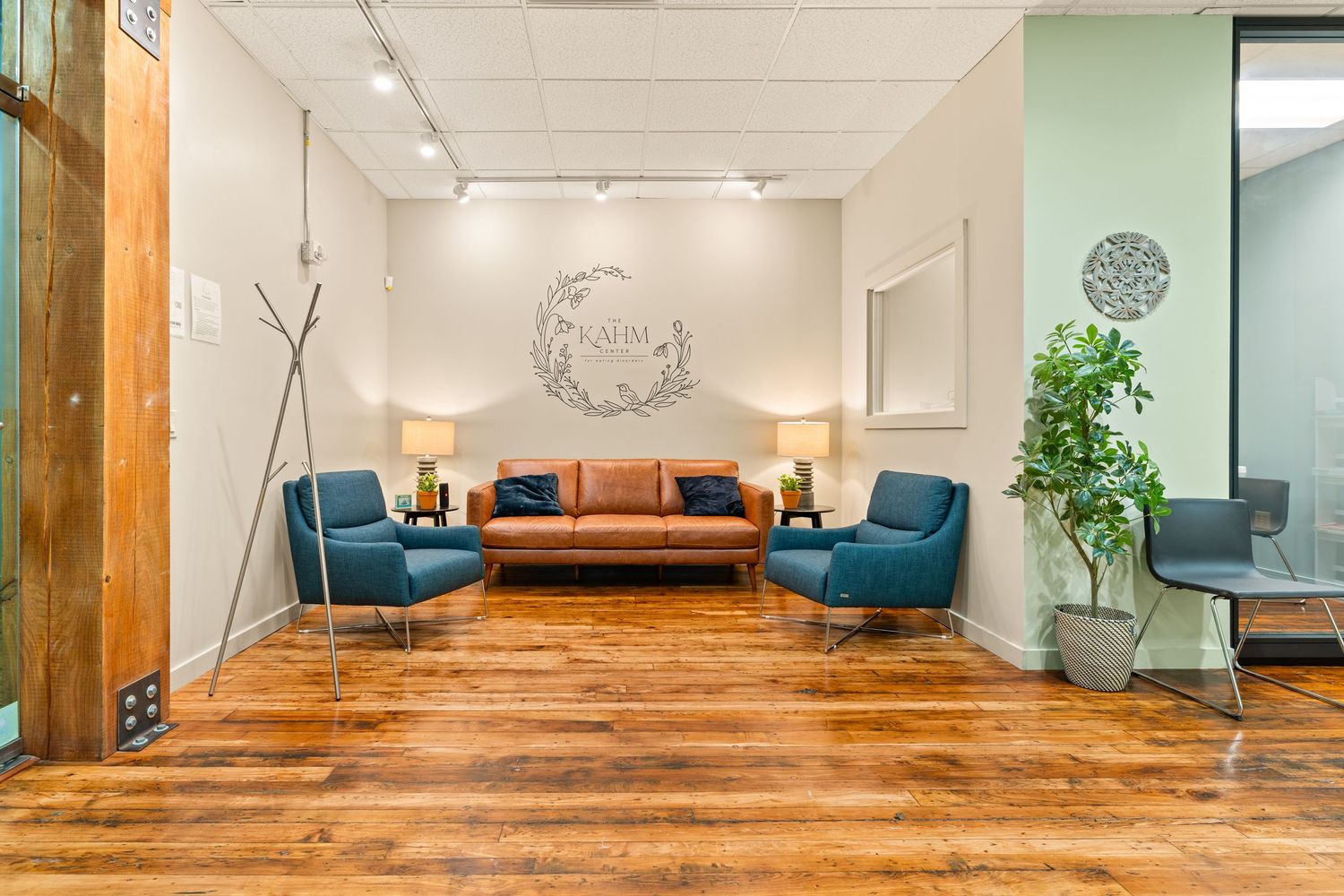 Modern office lounge with leather sofa, blue accent chairs, and warm wood flooring.