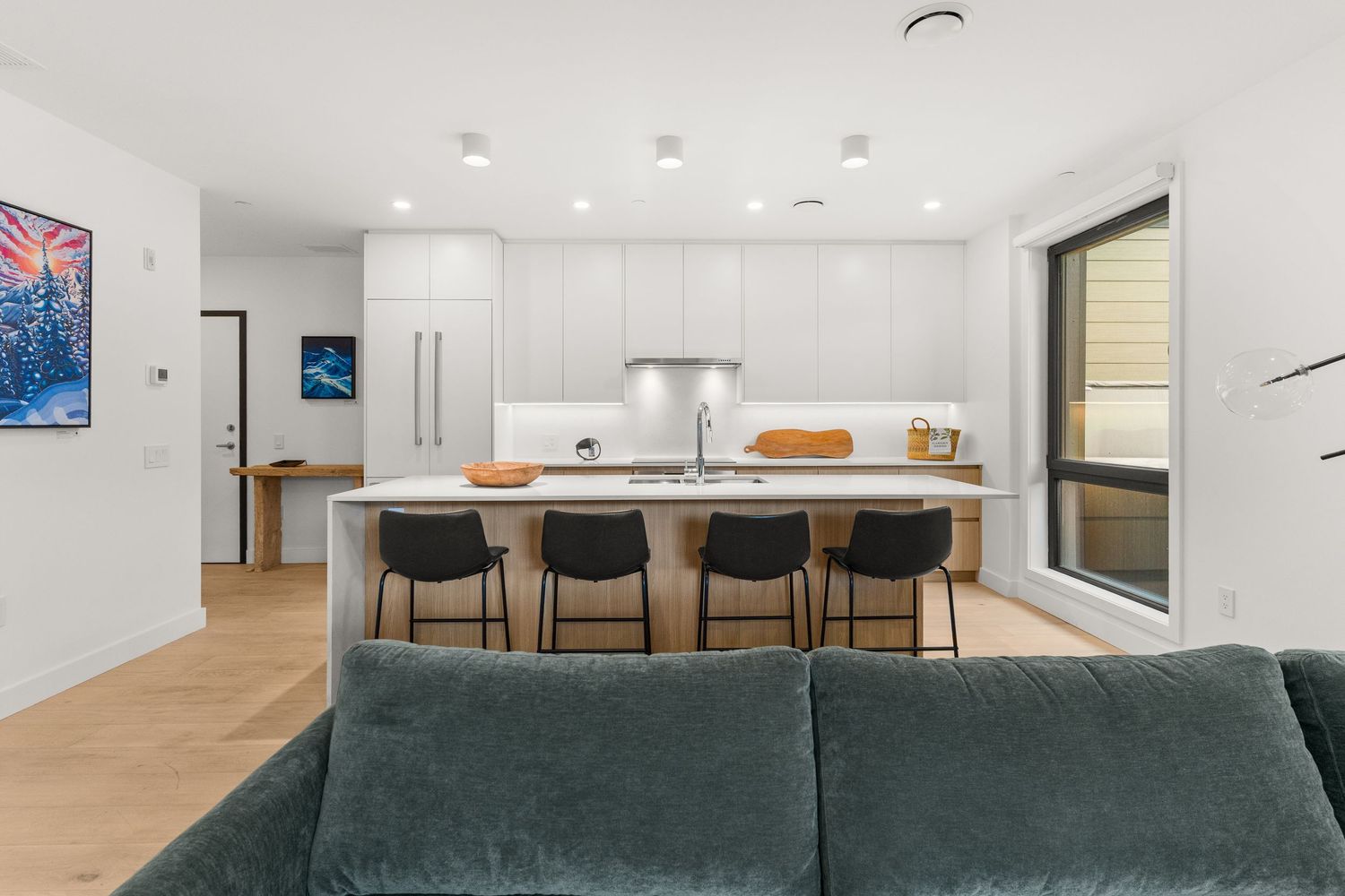 Modern open concept living room and kitchen with dark green sectional sofa, wood floors and recessed lighting.