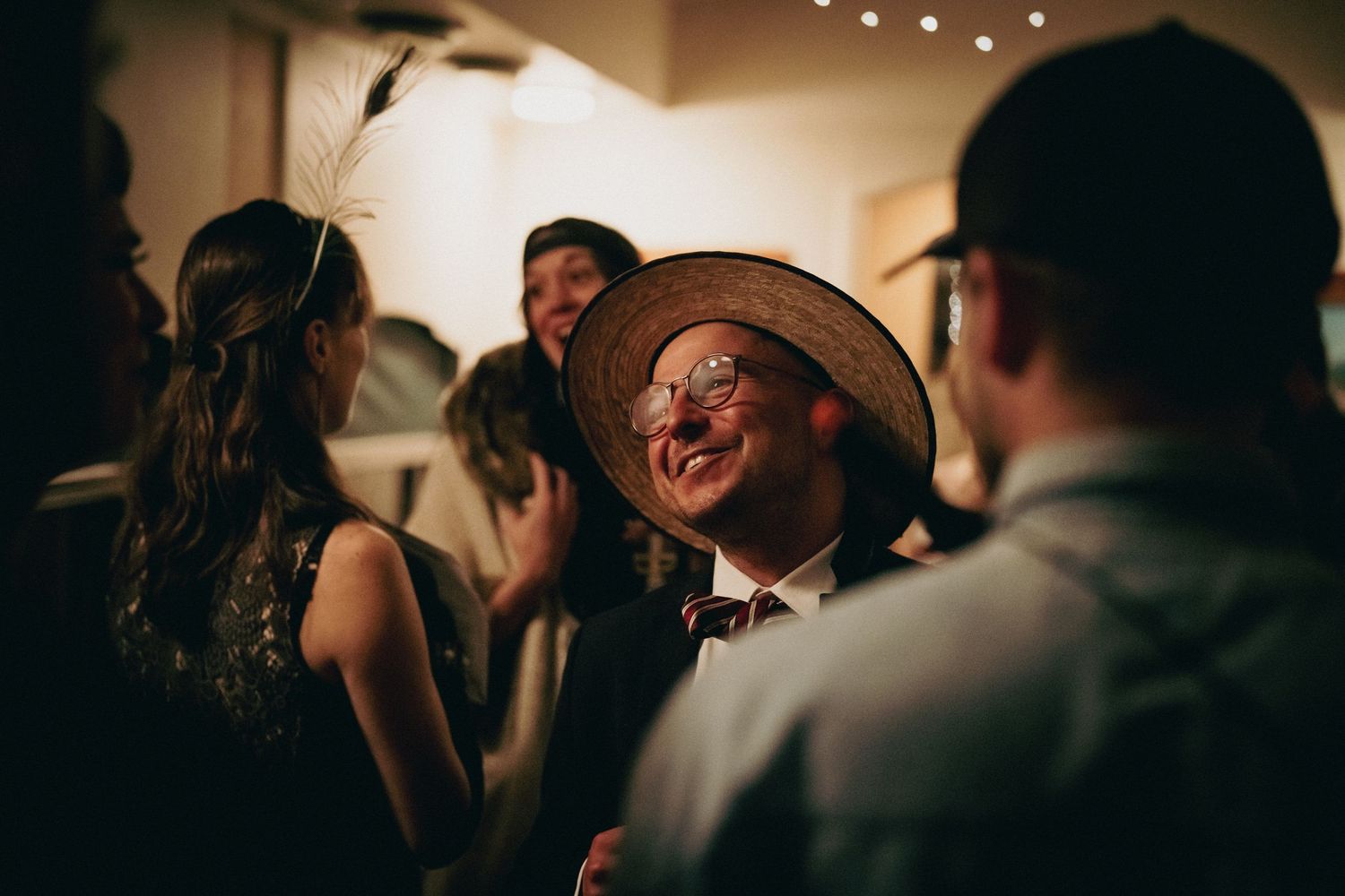 A dimly lit wedding reception venue with string lights overhead and guests mingling in the background.