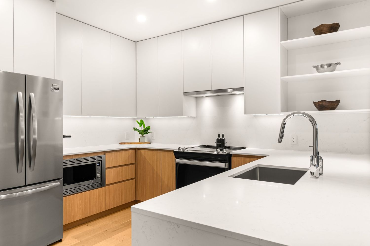 Modern kitchen with white countertops, wood cabinets, and stainless steel appliances in a bright, minimalist design.